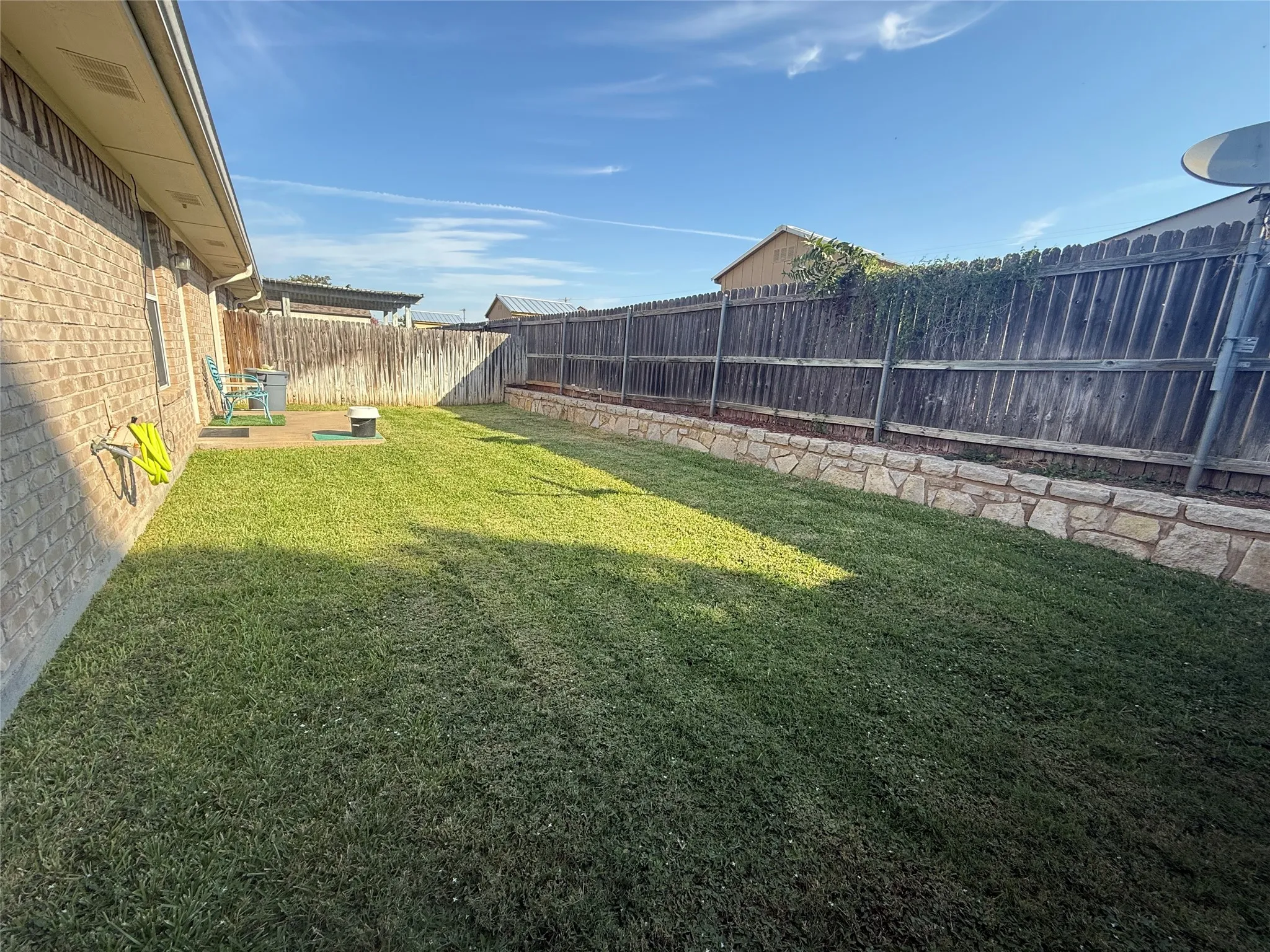 Expansive backyard featuring a manicured lawn, stone retaining wall, and a wood fence