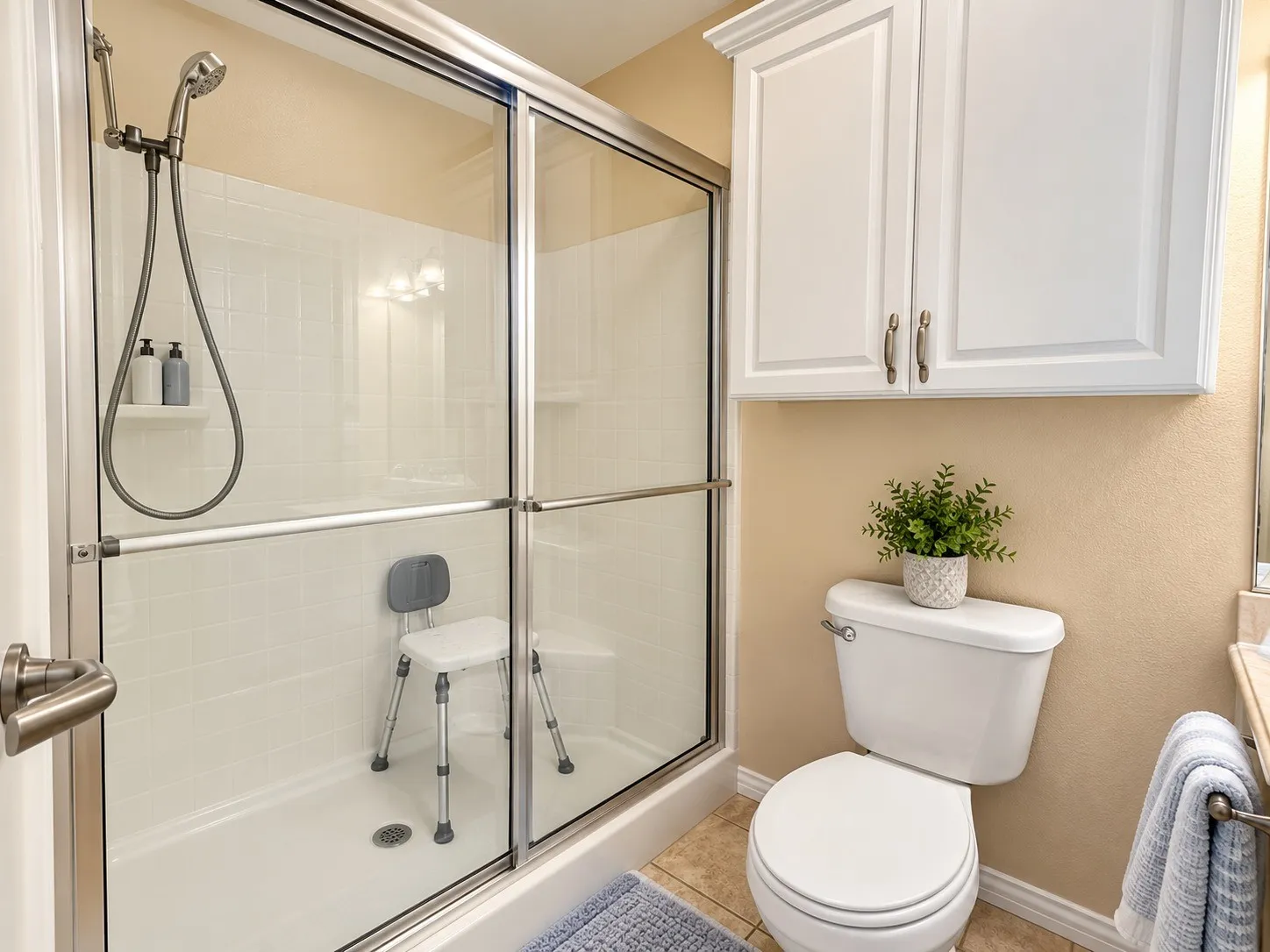 Glass-enclosed shower with a handheld shower head, white paneled cabinetry, and a toilet with tile flooring