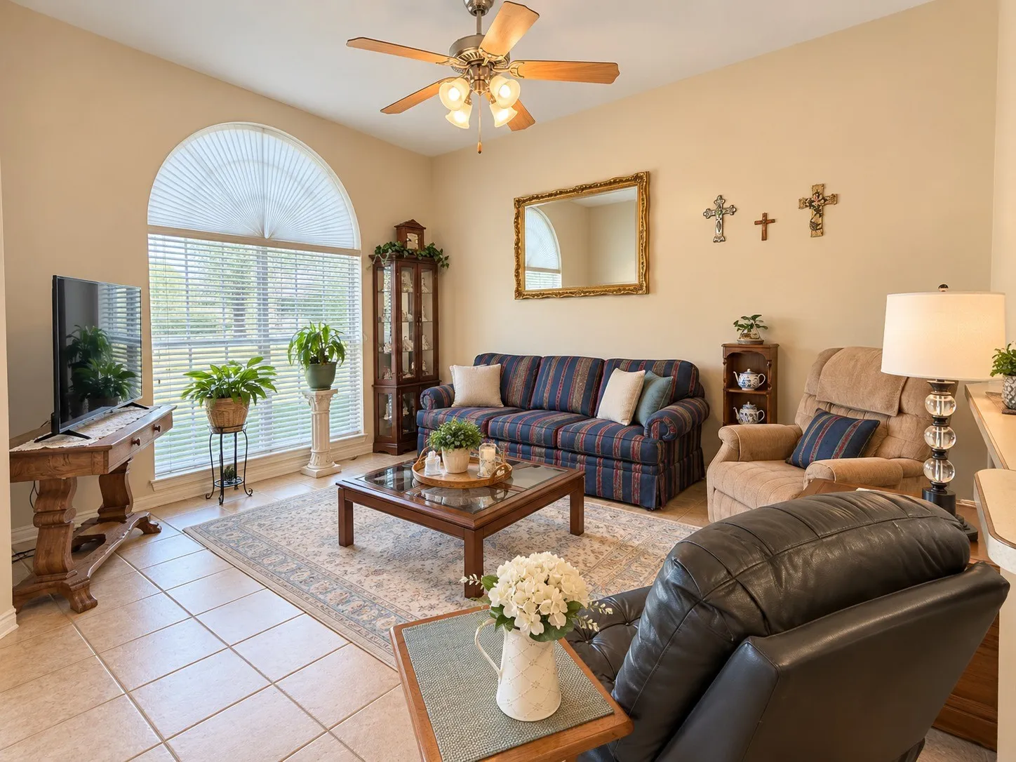 Tiled flooring throughout, featuring an arched window, a ceiling fan with light fixture, and a built-in display cabinet