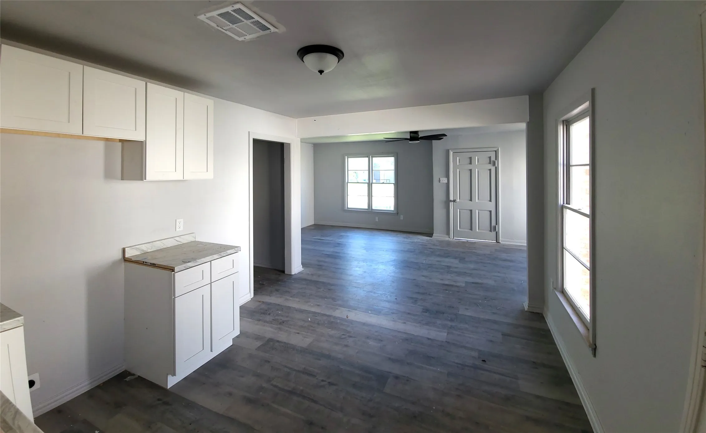 Kitchen with white cabinets, dark wood finished floors, ceiling fan, light countertops, and open floor plan