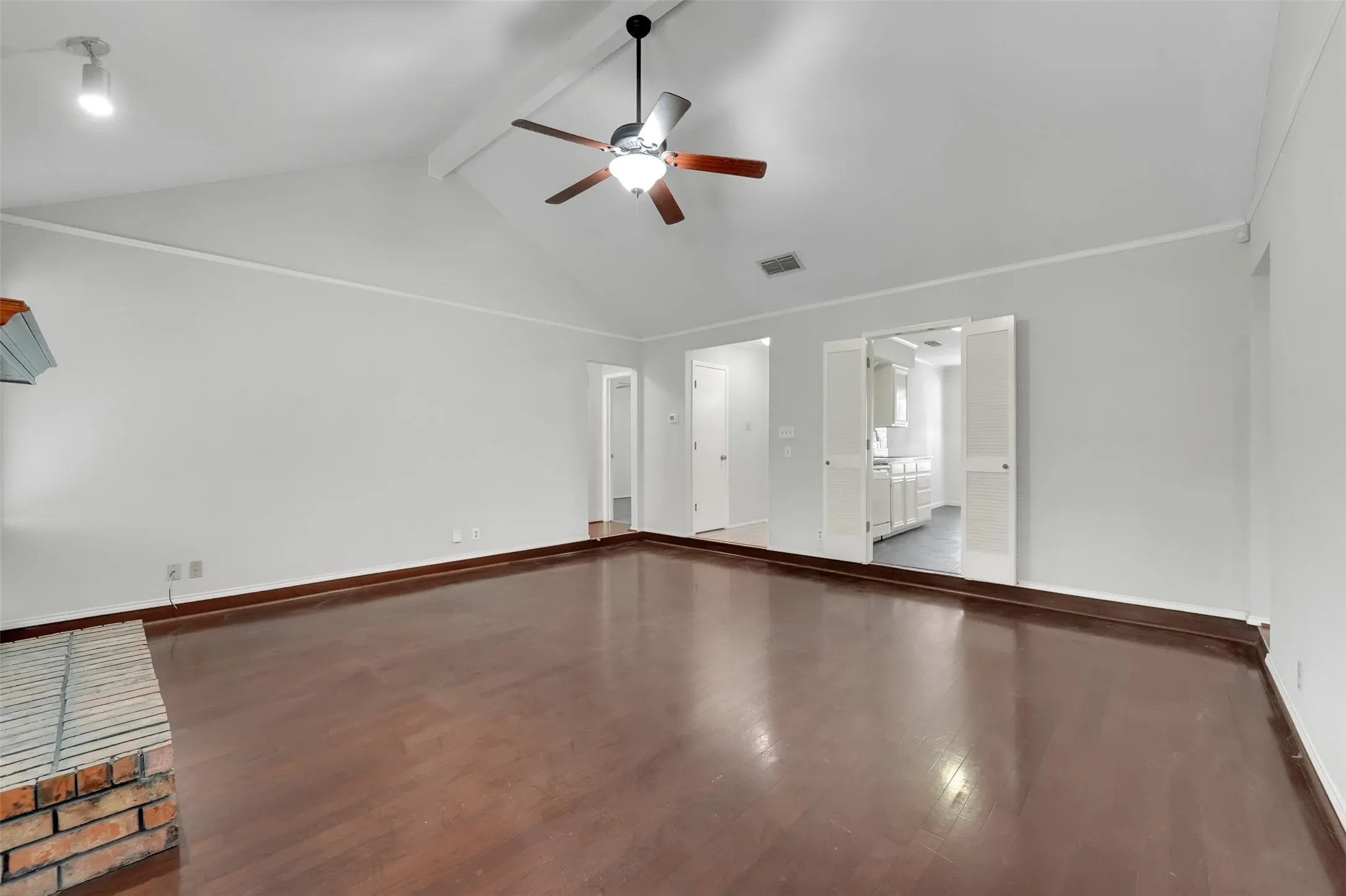 Vaulted ceiling with exposed beam, wood-finish flooring, brick fireplace, track lighting, and a ceiling fan with integrated lighting