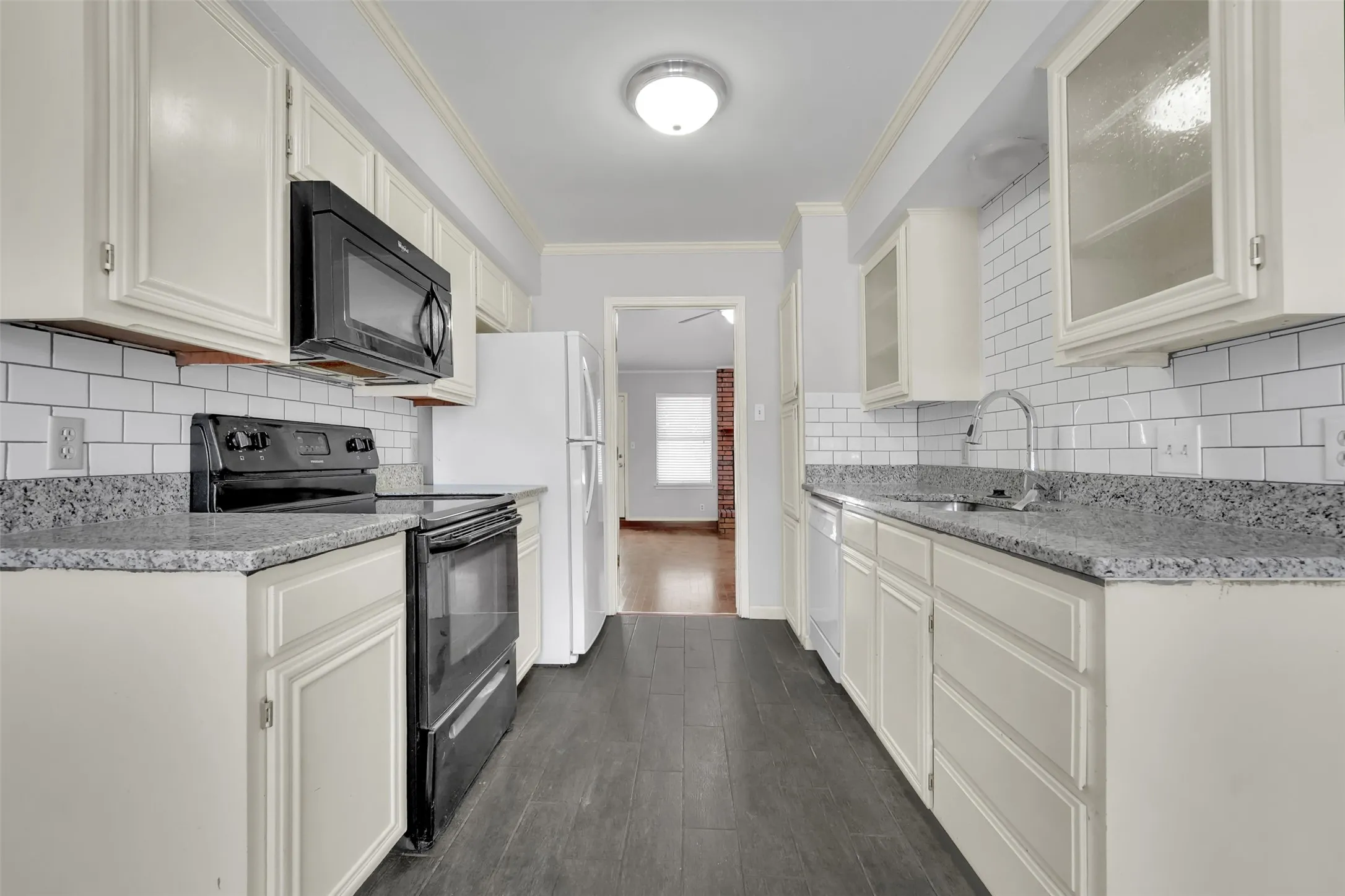 Galley kitchen featuring white cabinetry, subway tile backsplash, wood-finish flooring, and light-colored countertops