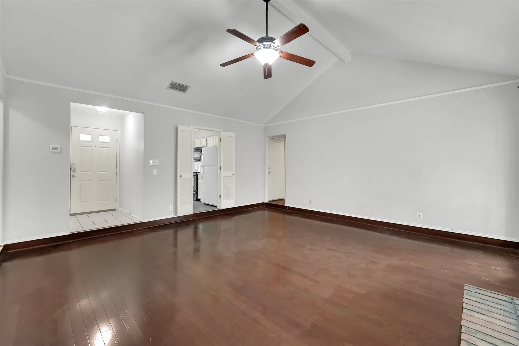 Vaulted ceiling with exposed beam, wood-finish flooring, ceiling fan with integrated lighting, white entry door with frosted glass panels, and double bifold doors