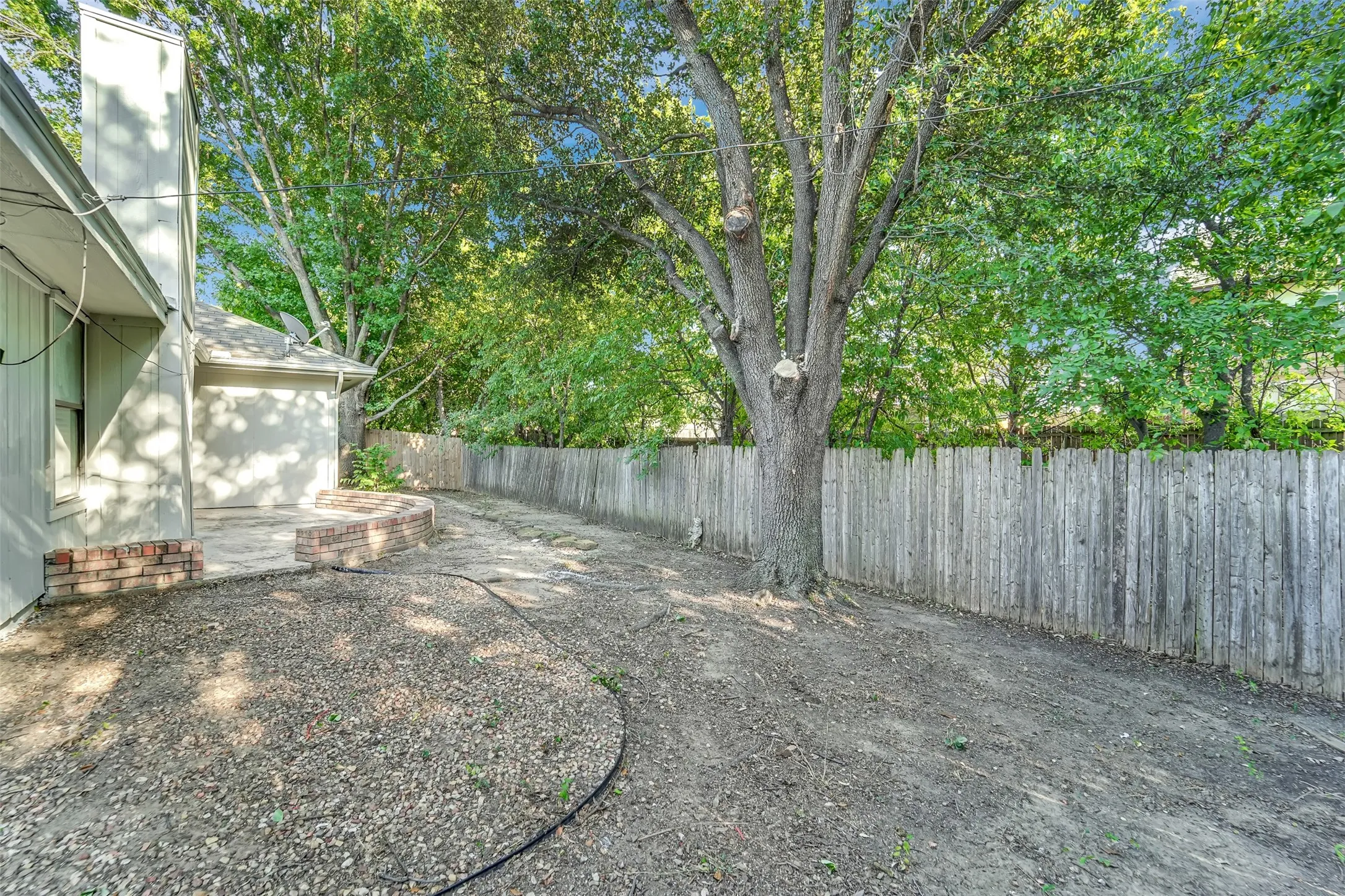 Outdoor patio with brick border, privacy fencing, and mature trees