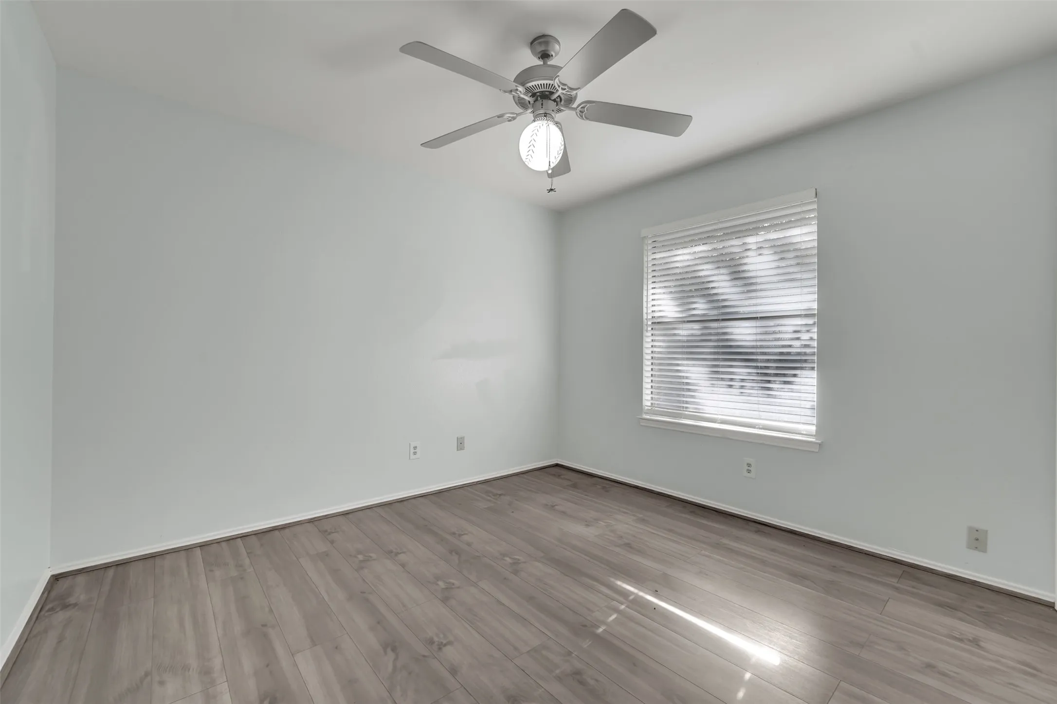 Recessed window with horizontal blinds, overhead ceiling fan with lighting fixture, wood-finish flooring, and light-colored walls