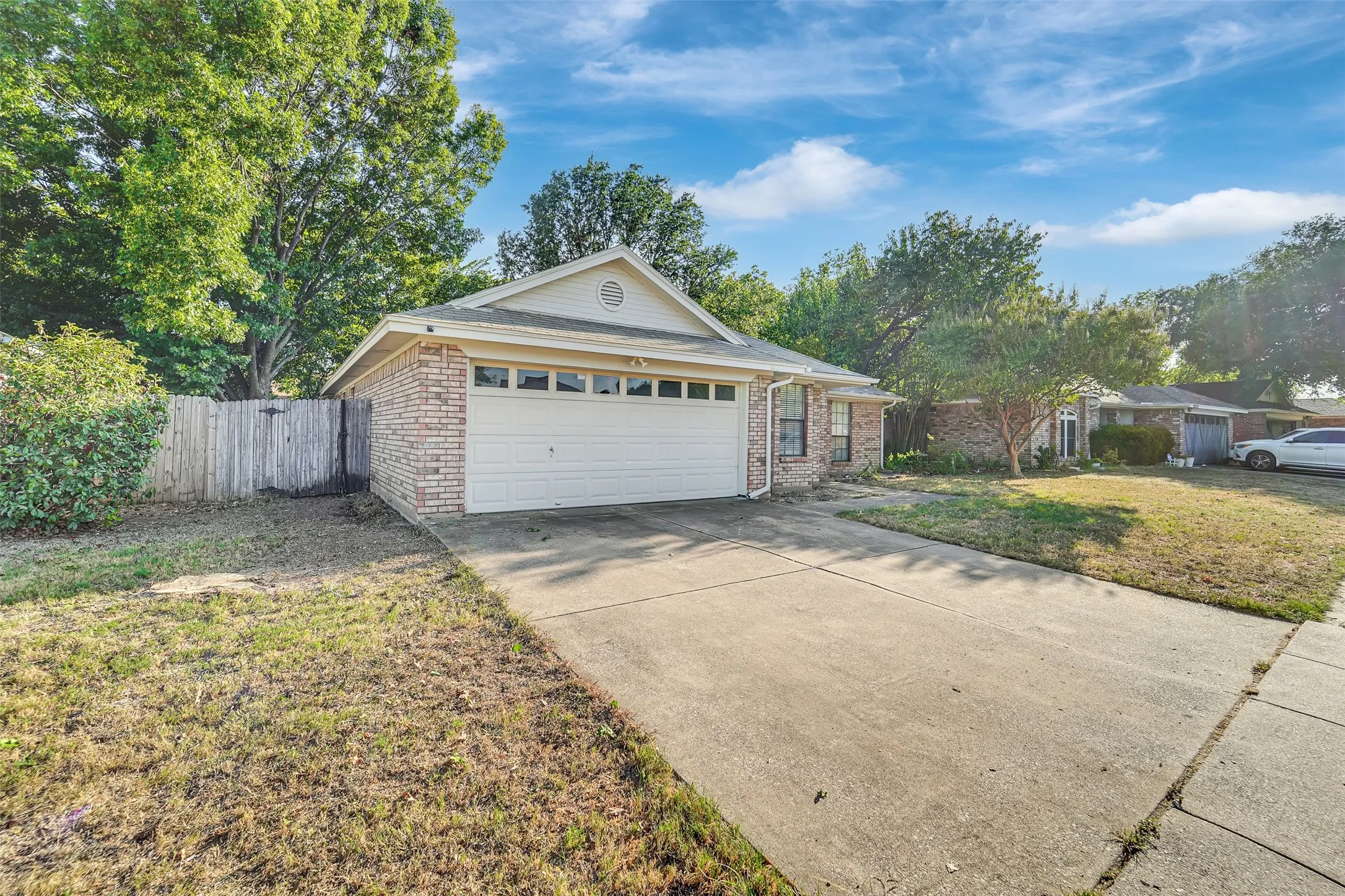 Brick exterior home with an attached garage, featuring a concrete driveway and an enclosed side yard with a wood fence