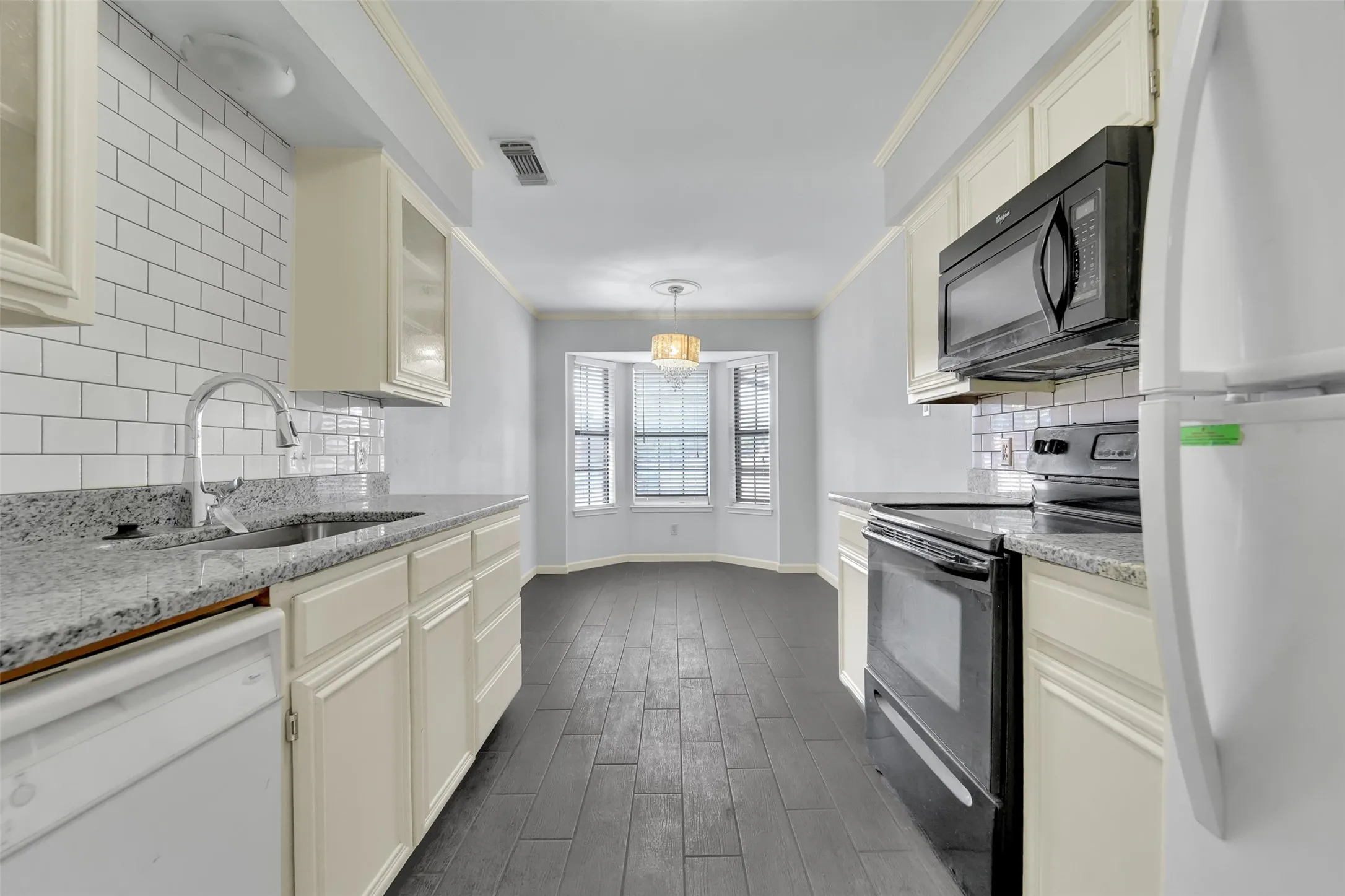 Kitchen featuring white subway tile backsplash, light-toned cabinetry, and dark wood-finish flooring