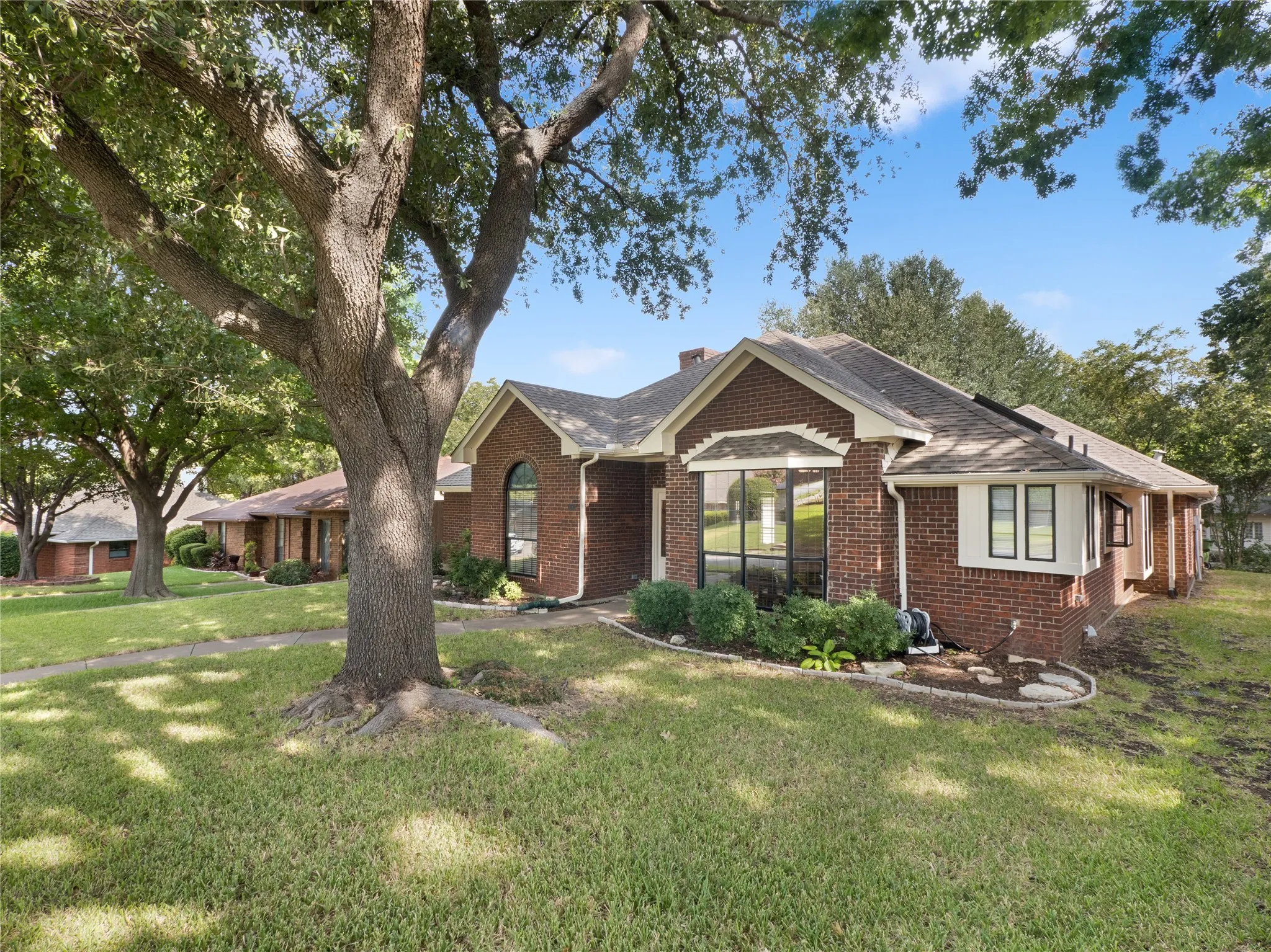 Brick exterior with a prominent bay window, established landscaping, arched window detail, and mature tree