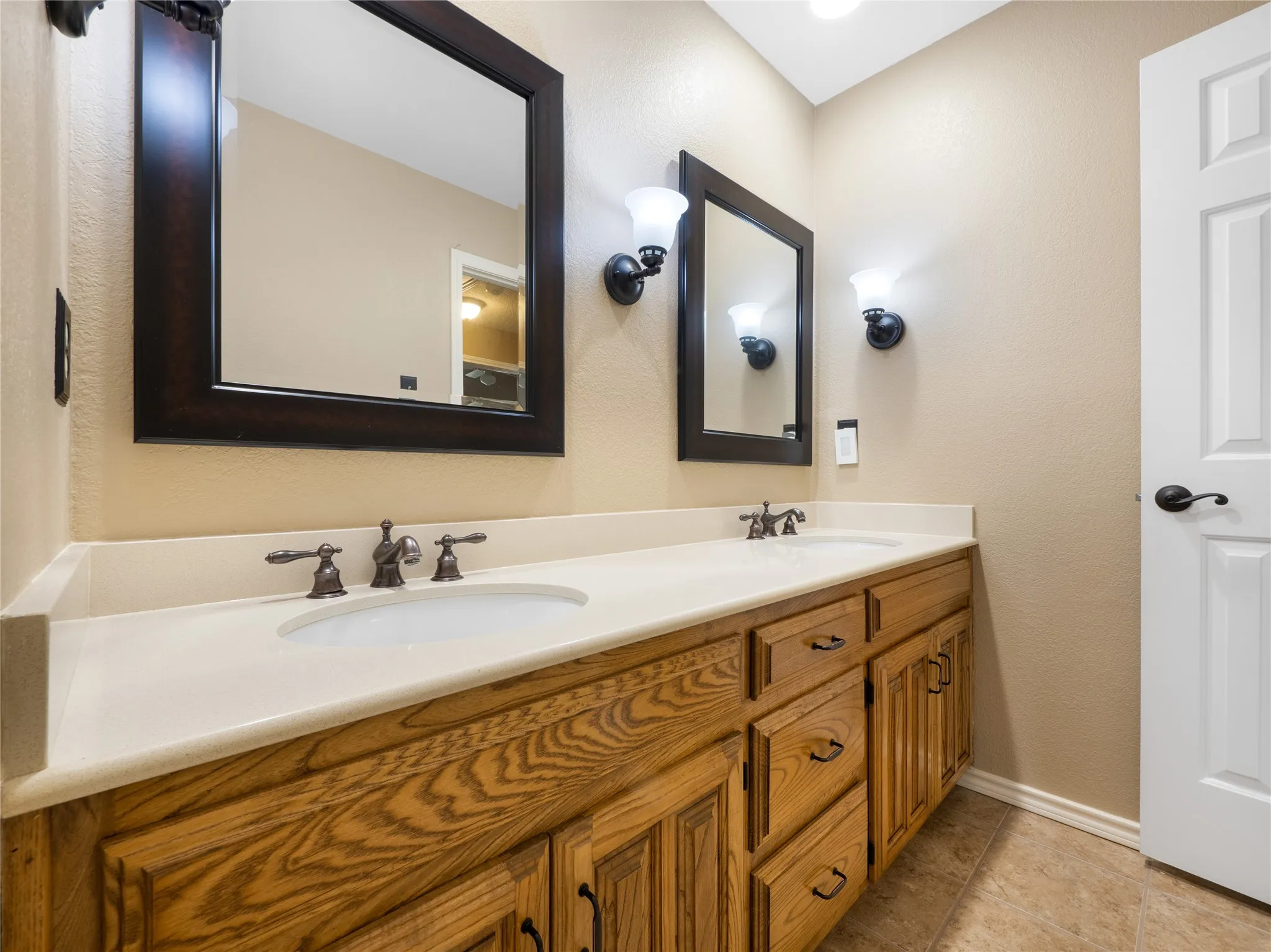Secondary bathroom with double vanity with wood-finish cabinetry, integrated sinks, white countertop, and individual mirrors with wall-mounted lighting