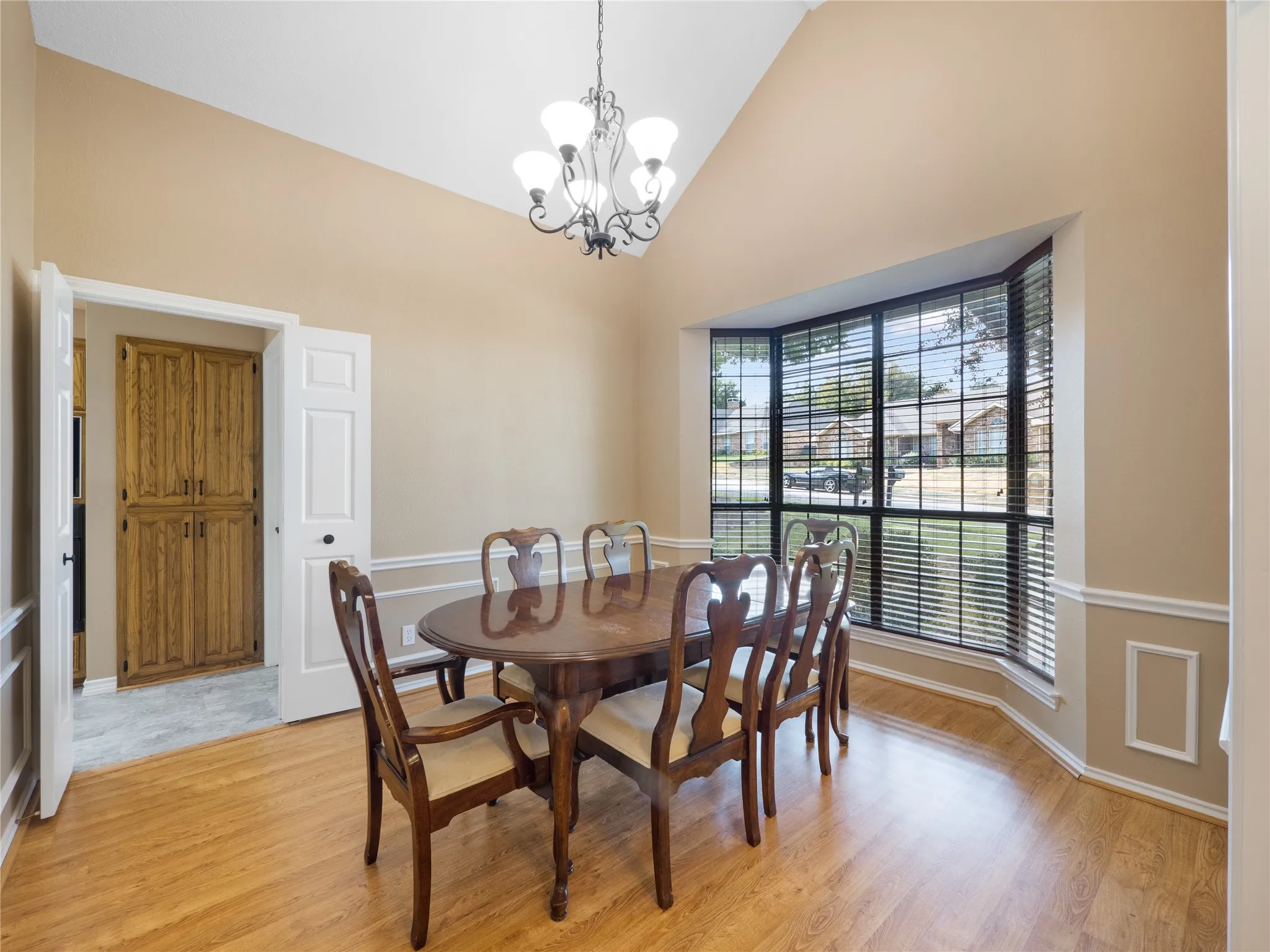 Vaulted ceiling, chandelier, expansive bay window, wood-finish flooring, and built-in wood cabinetry