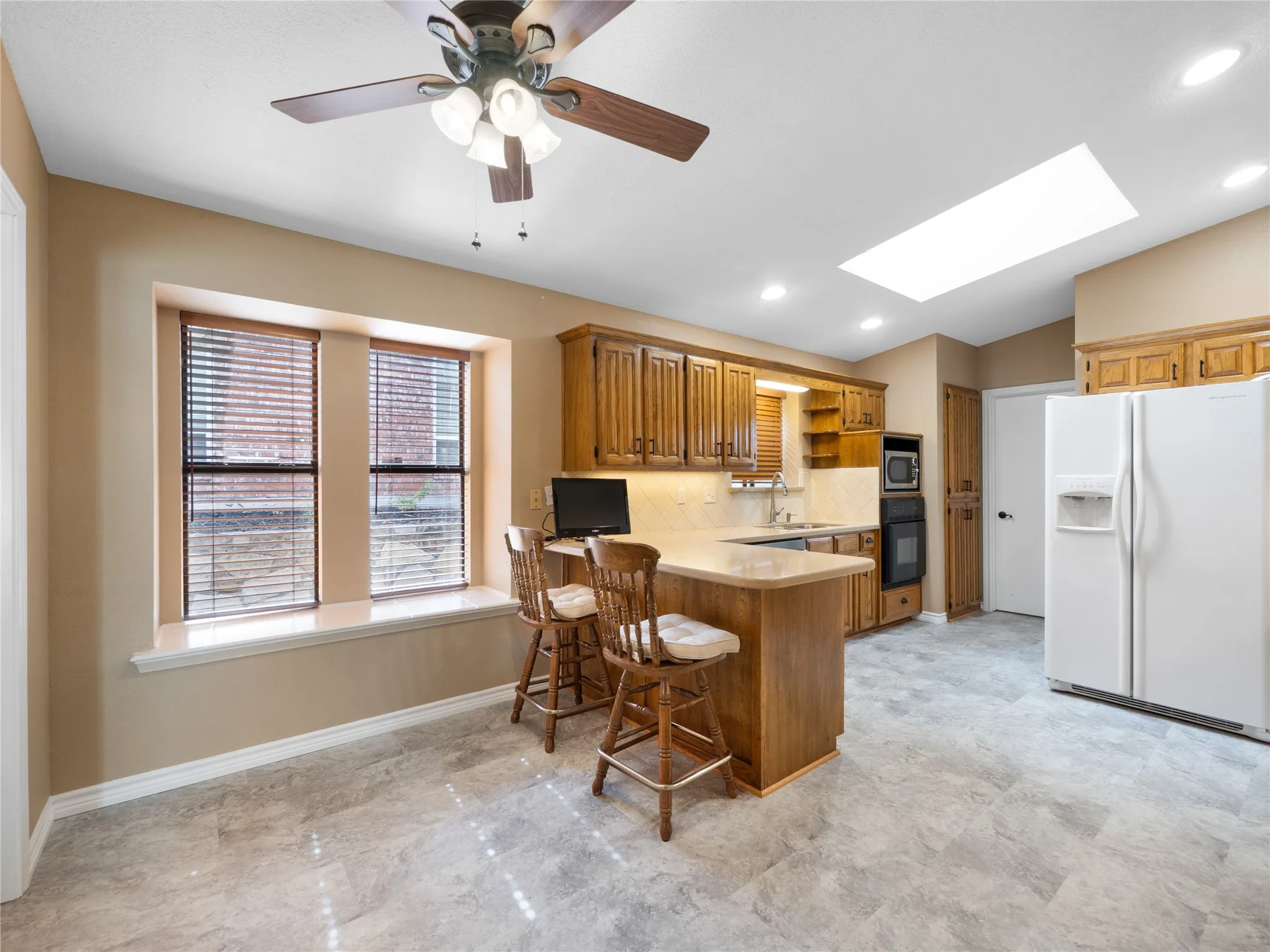 Kitchen featuring wood cabinetry, a breakfast bar, stone-finish flooring, a ceiling fan with integrated lighting, and a skylight