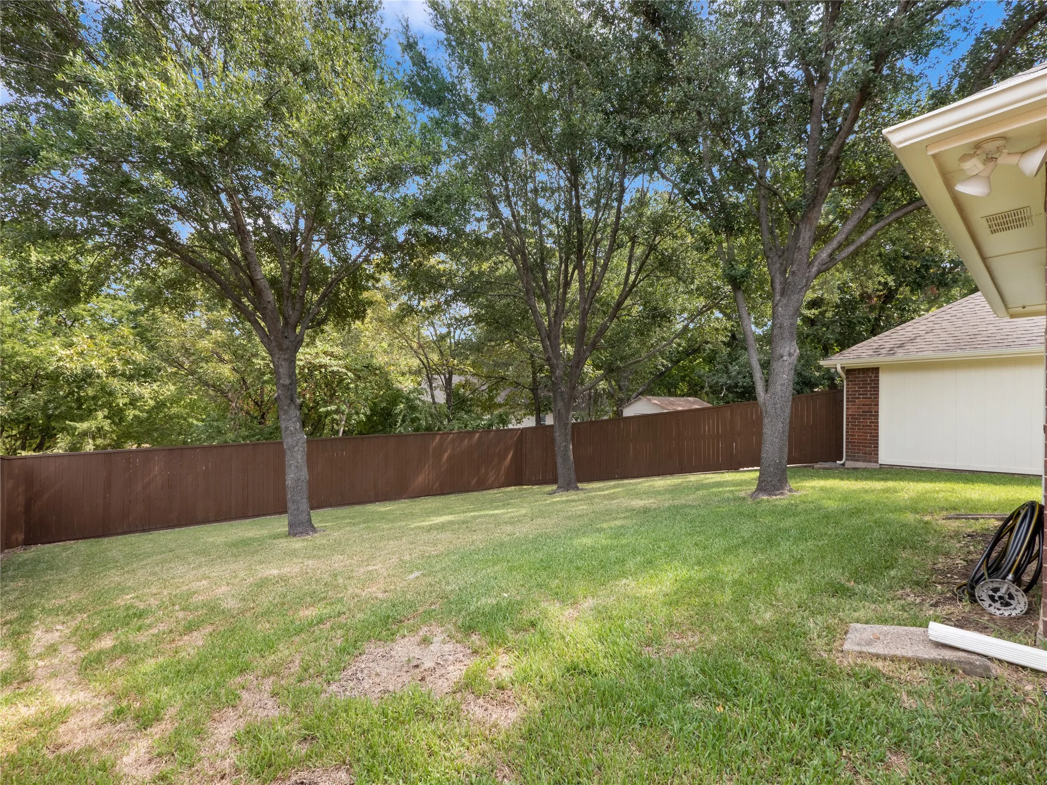 Backyard featuring mature trees, a wooden privacy fence, and an exterior brick and siding wall