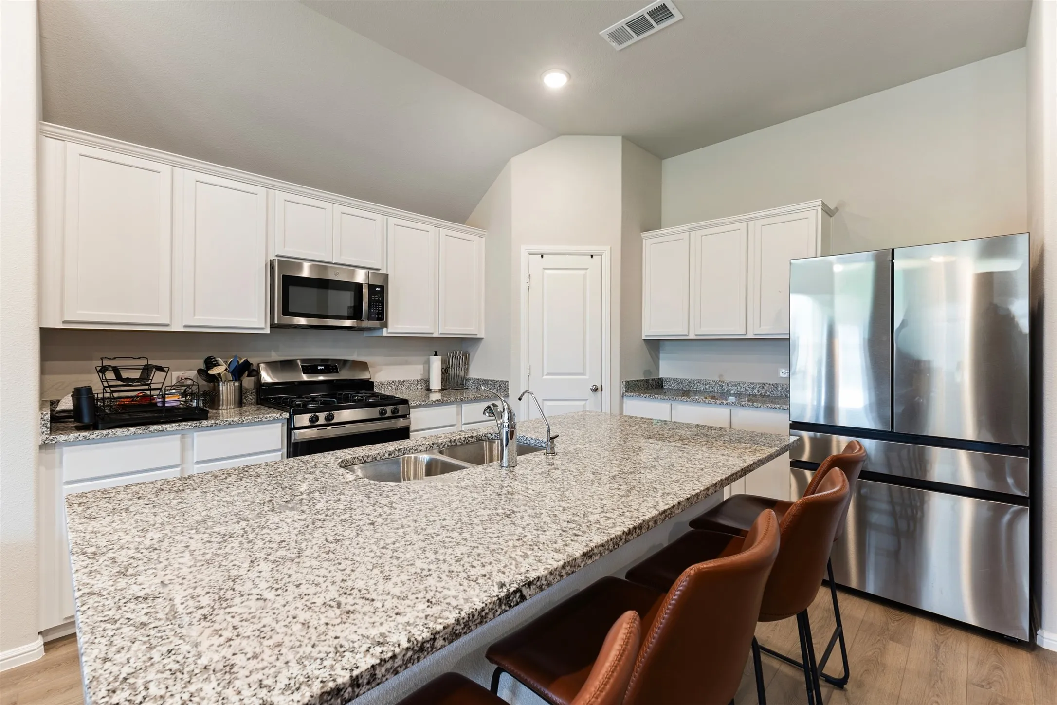 Kitchen with appliances with stainless steel finishes, white cabinets, light wood finished floors, light stone counters, and a kitchen bar