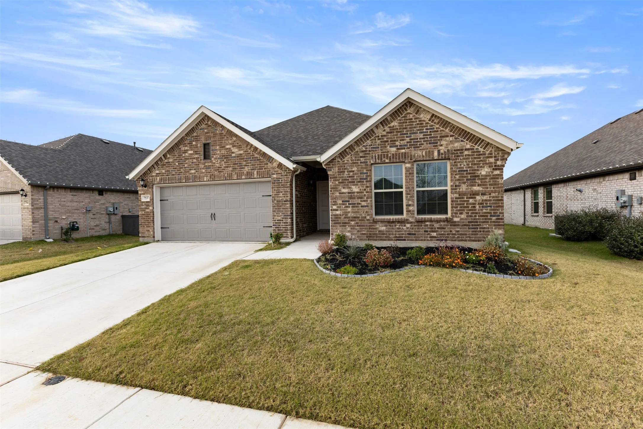 View of front of home with brick siding, a front lawn, driveway, a shingled roof, and a garage