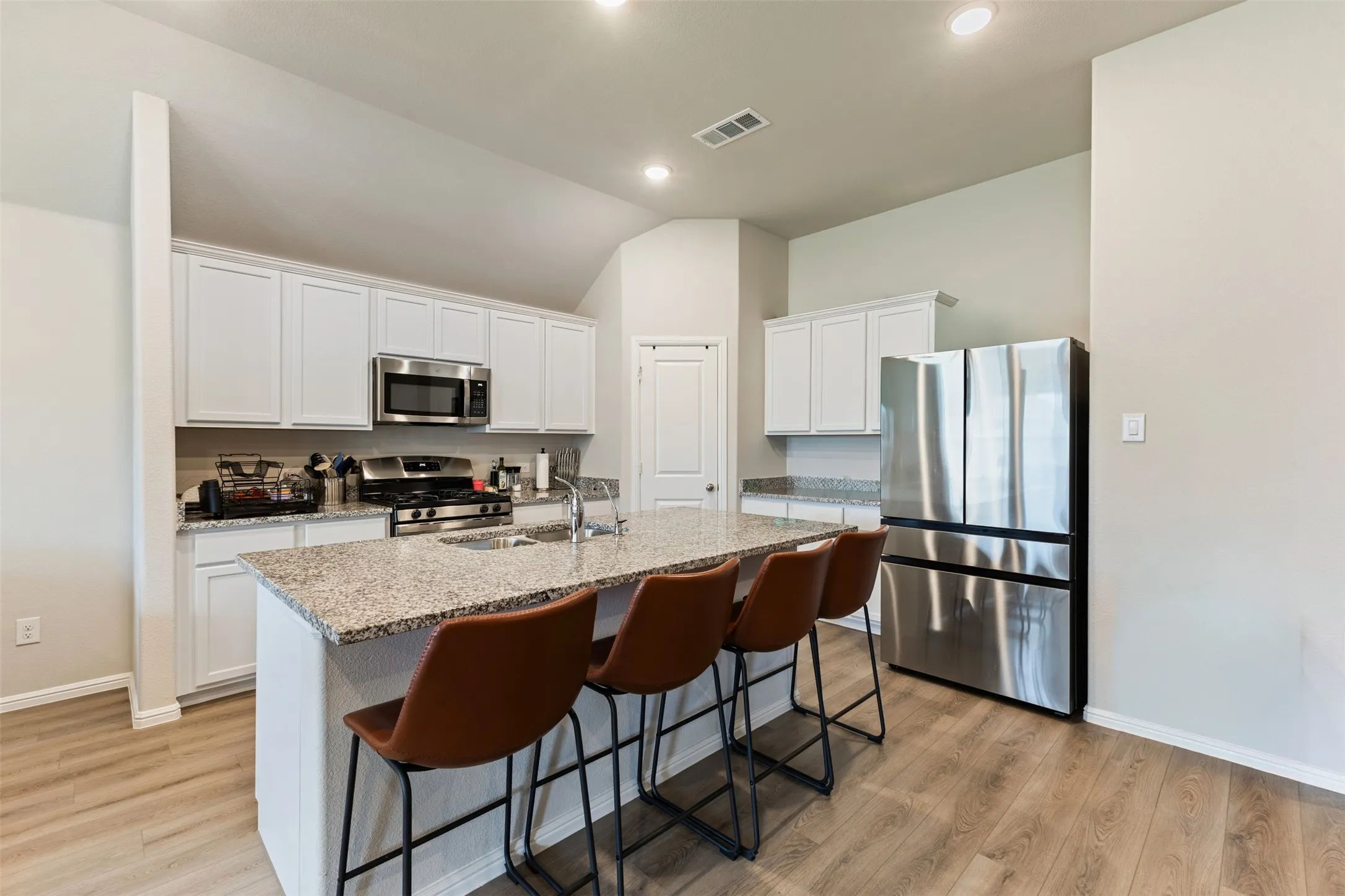 Kitchen with appliances with stainless steel finishes, white cabinetry, light stone counters, a breakfast bar, and a kitchen island with sink