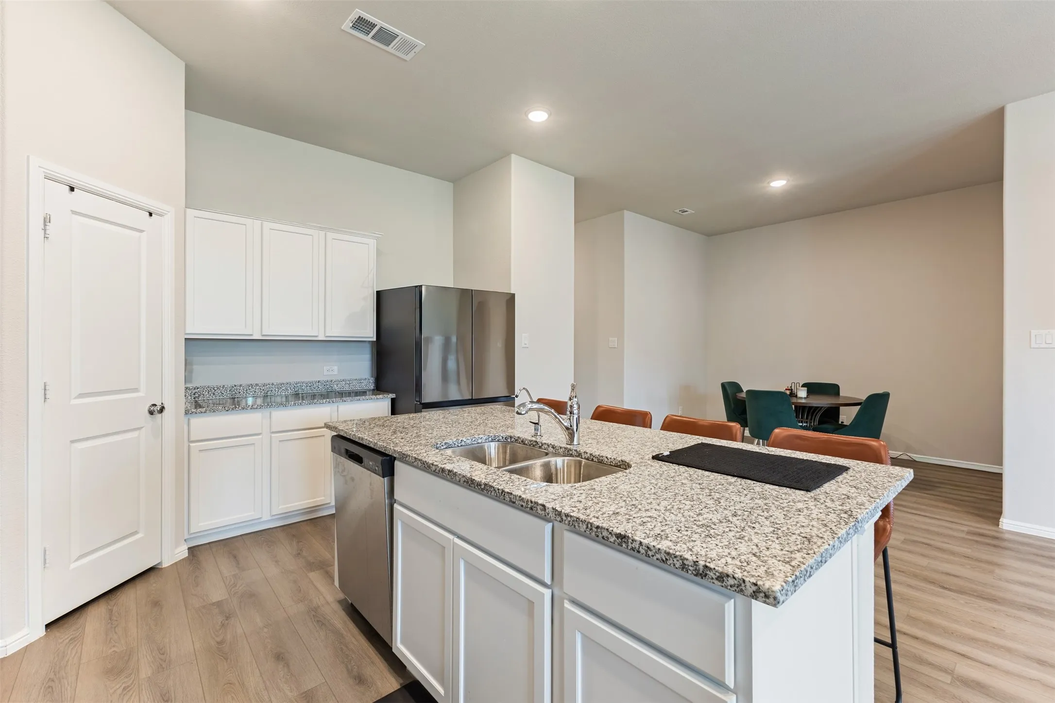 Kitchen featuring a breakfast bar, white cabinetry, light stone counters, stainless steel appliances, and a kitchen island with sink