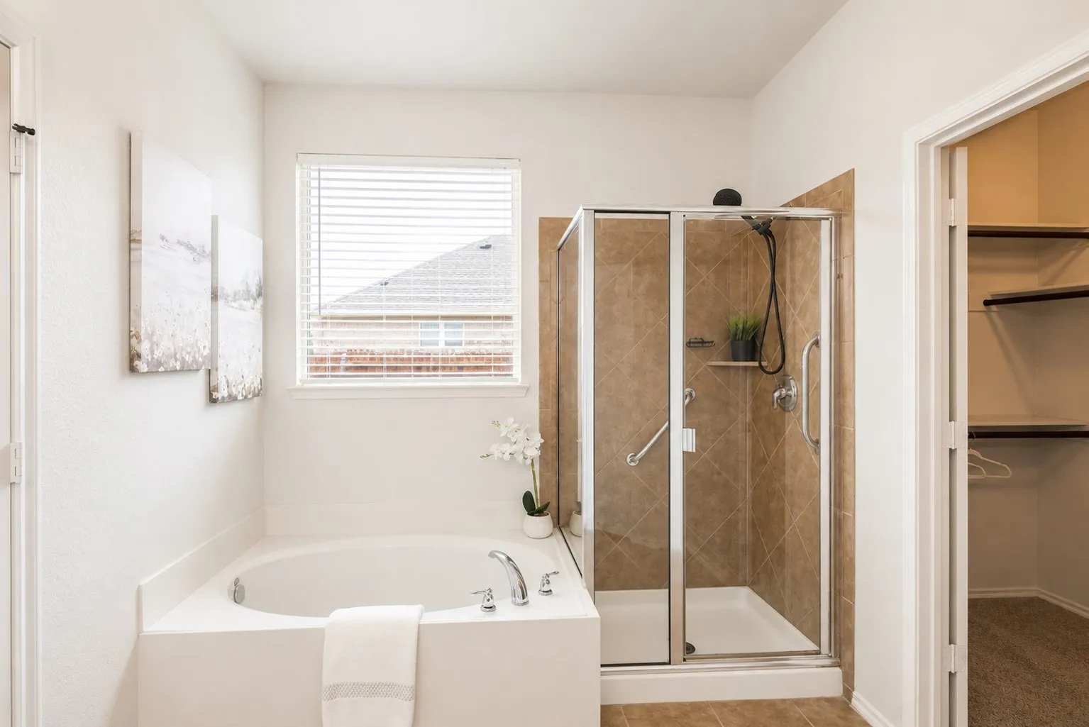 Built-in soaking tub with chrome fixtures, enclosed shower with tile surround, and an adjacent walk-in closet with shelving