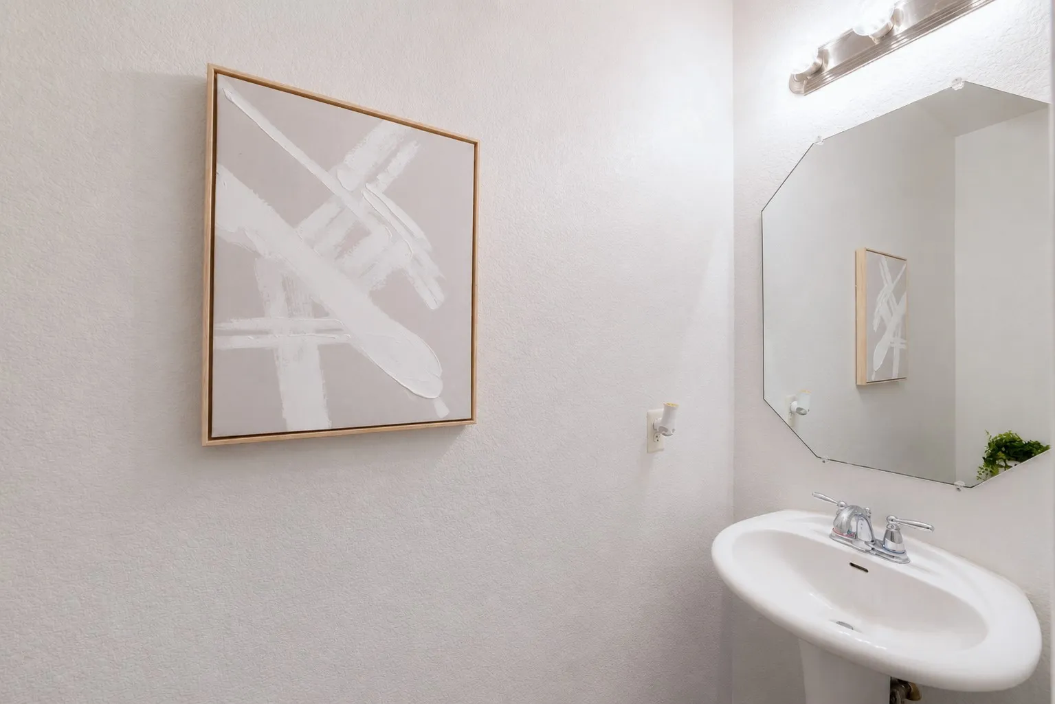 White pedestal sink with chrome faucet, octagonal wall mirror, and wall-mounted vanity lighting