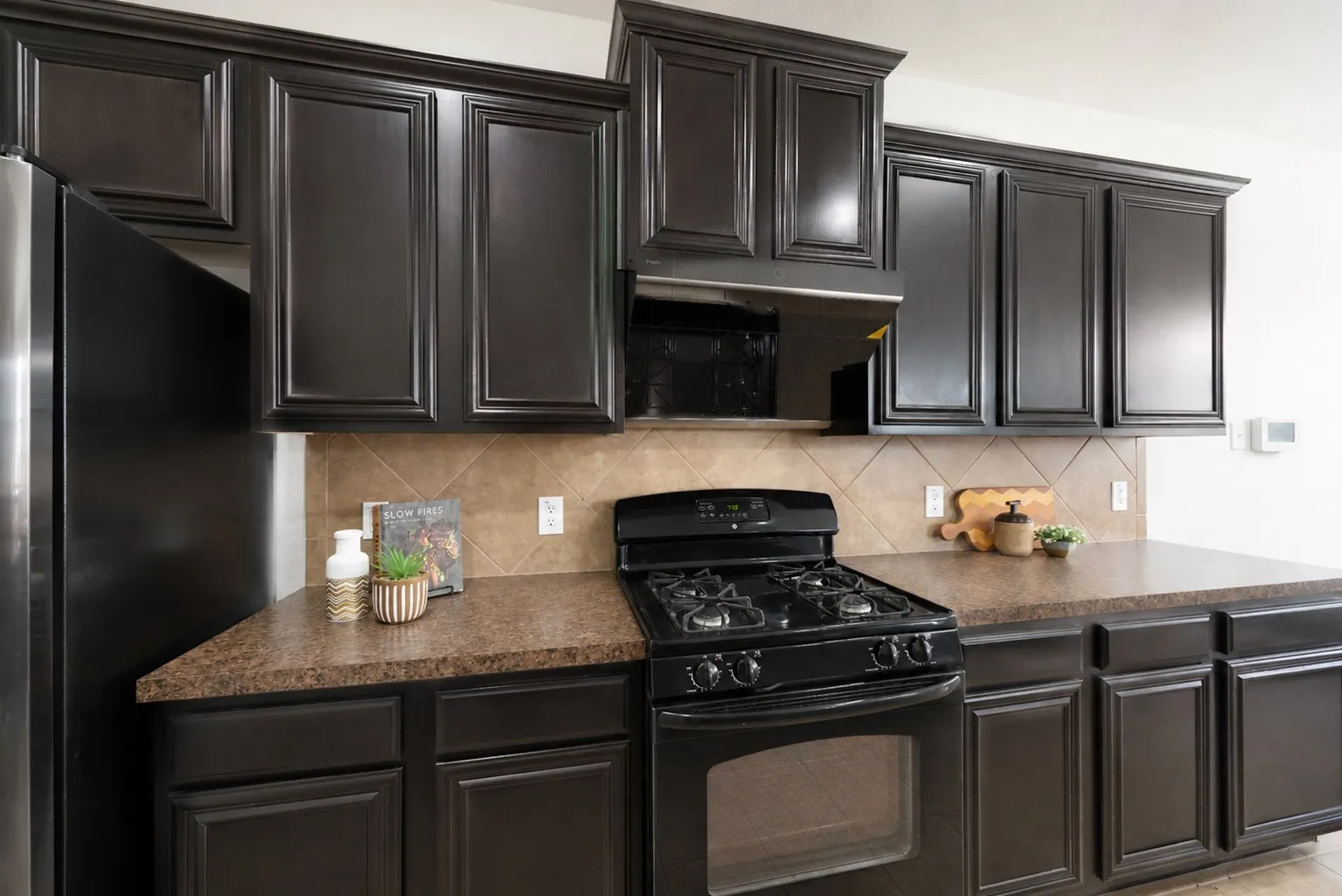 Dark wood-finish cabinetry, patterned backsplash tiling, built-in oven, and a black gas range