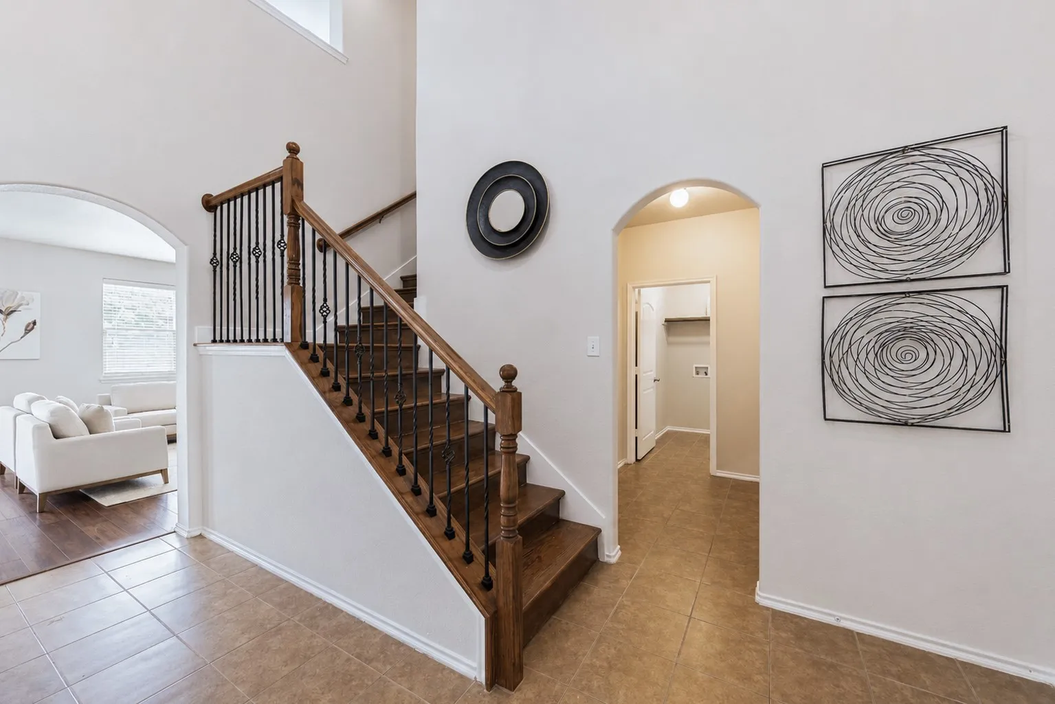 Hardwood staircase with wrought iron balusters, tile flooring, and arched doorways