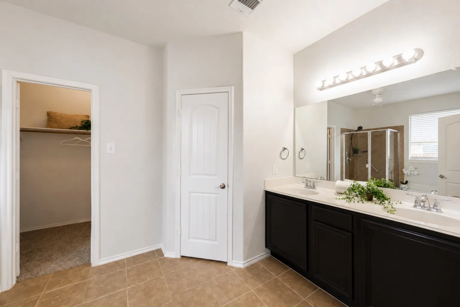 Dual vanity with an expansive mirror, enclosed shower, and tile flooring