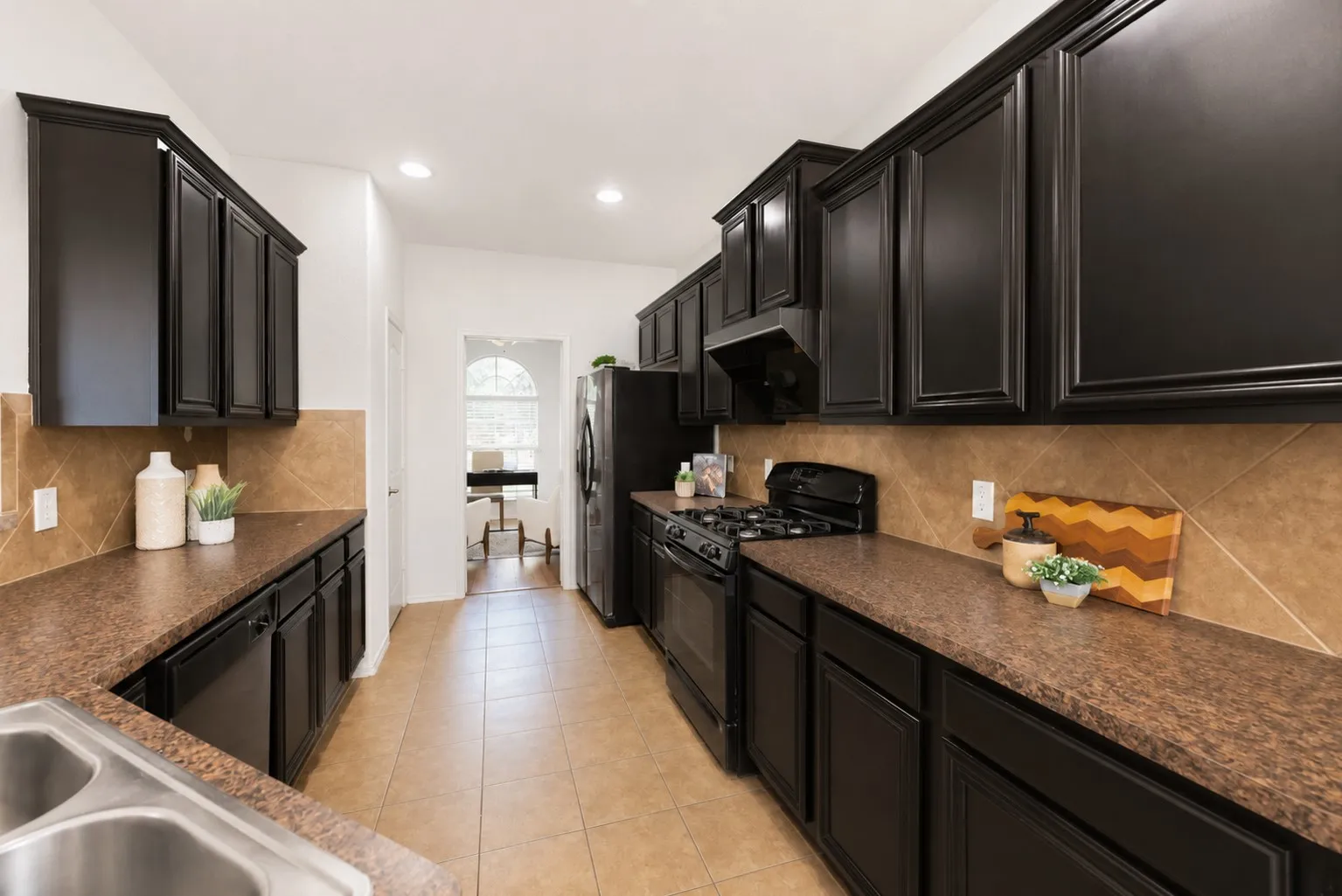 Kitchen featuring dark wood cabinetry, a gas range, a stainless steel double basin sink, light-toned tile flooring, and recessed lighting
