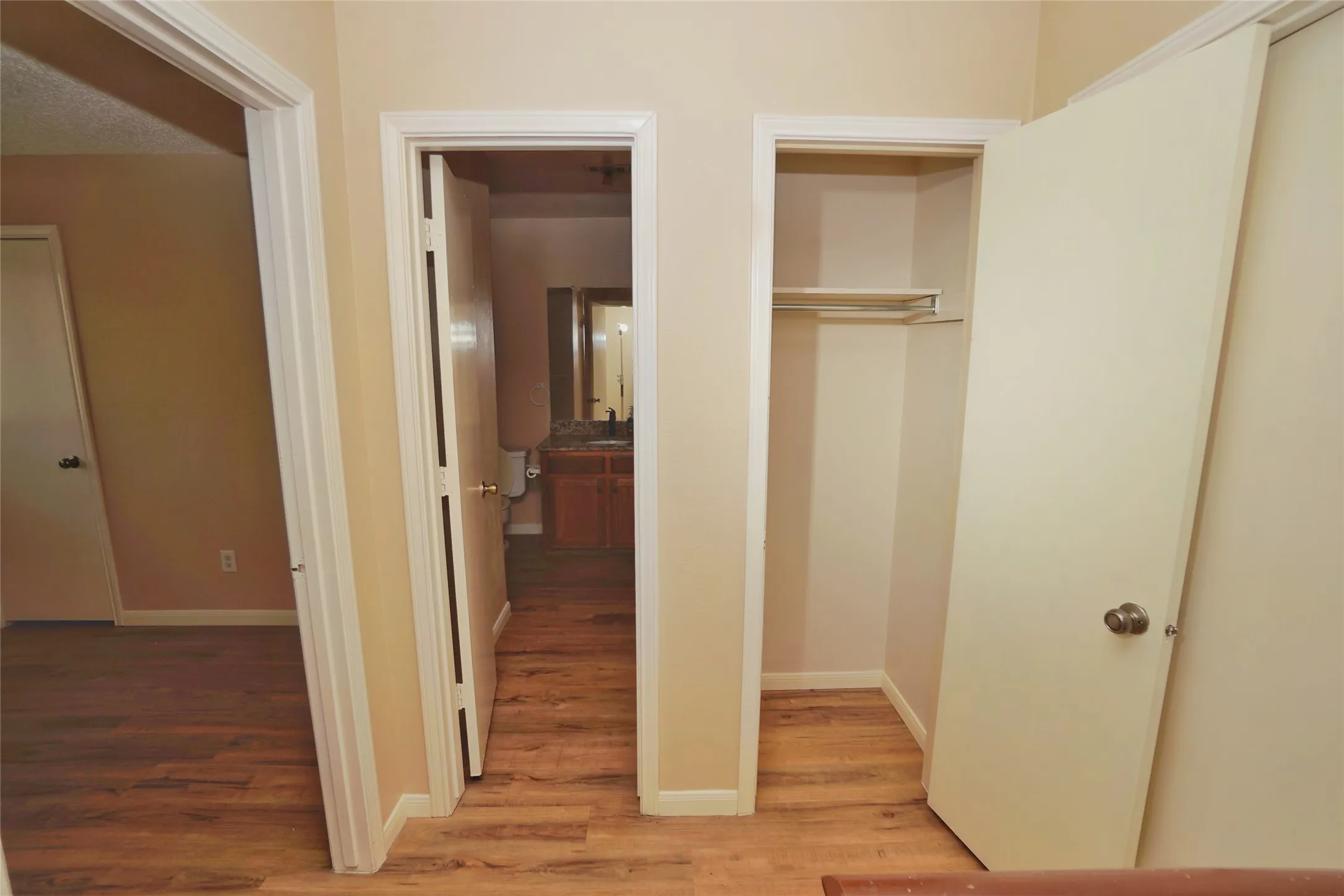 Wood-finish flooring throughout, white trim, and a built-in closet with shelving and hanging rod
