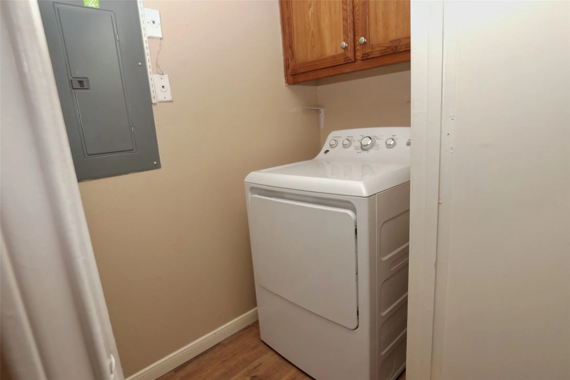 Laundry area featuring a large capacity dryer, wood-finish flooring, and upper cabinetry