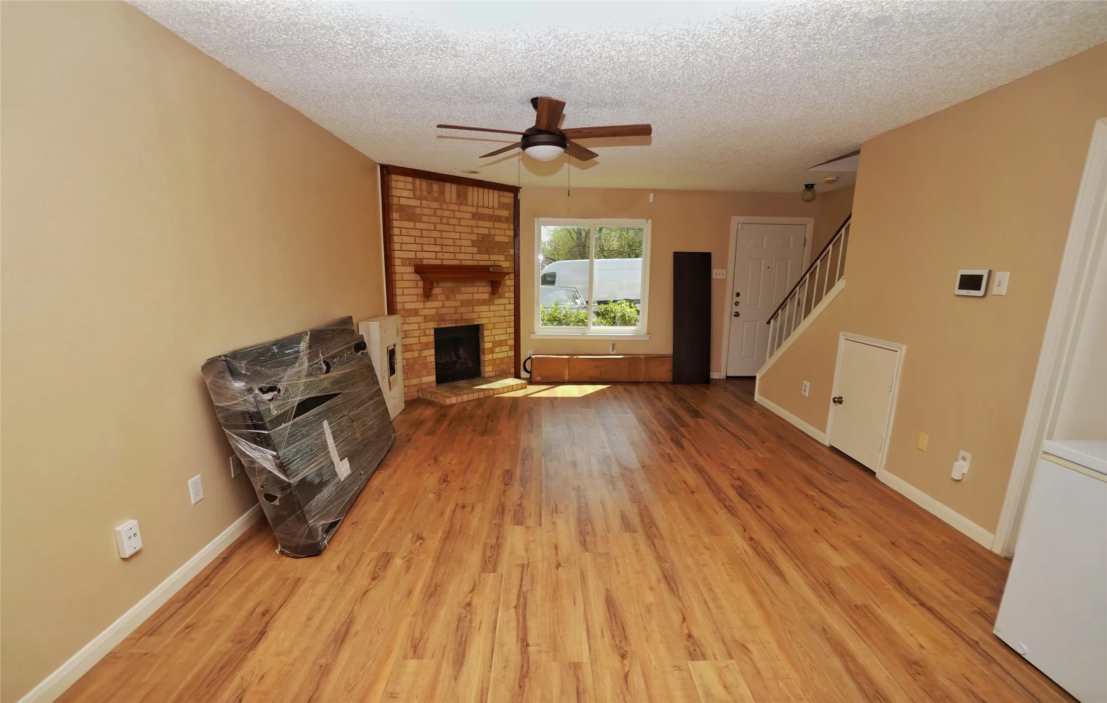 Spacious living area featuring wood-finish flooring, a brick fireplace with a mantle, and a ceiling fan