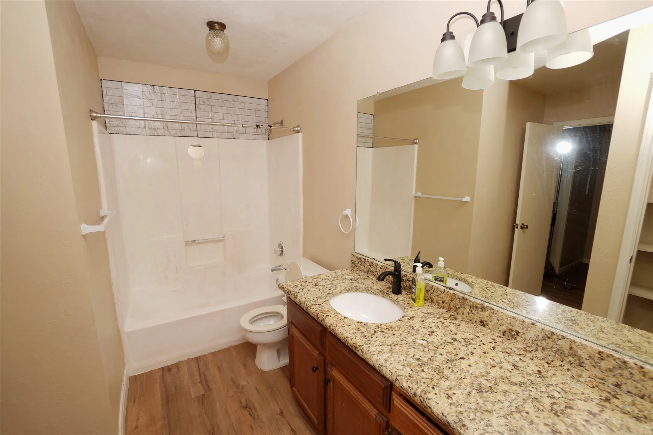 Bathroom featuring a vanity with a granite-style countertop, a white basin, a dark finish faucet, a full-width mirror, and wood-finish flooring