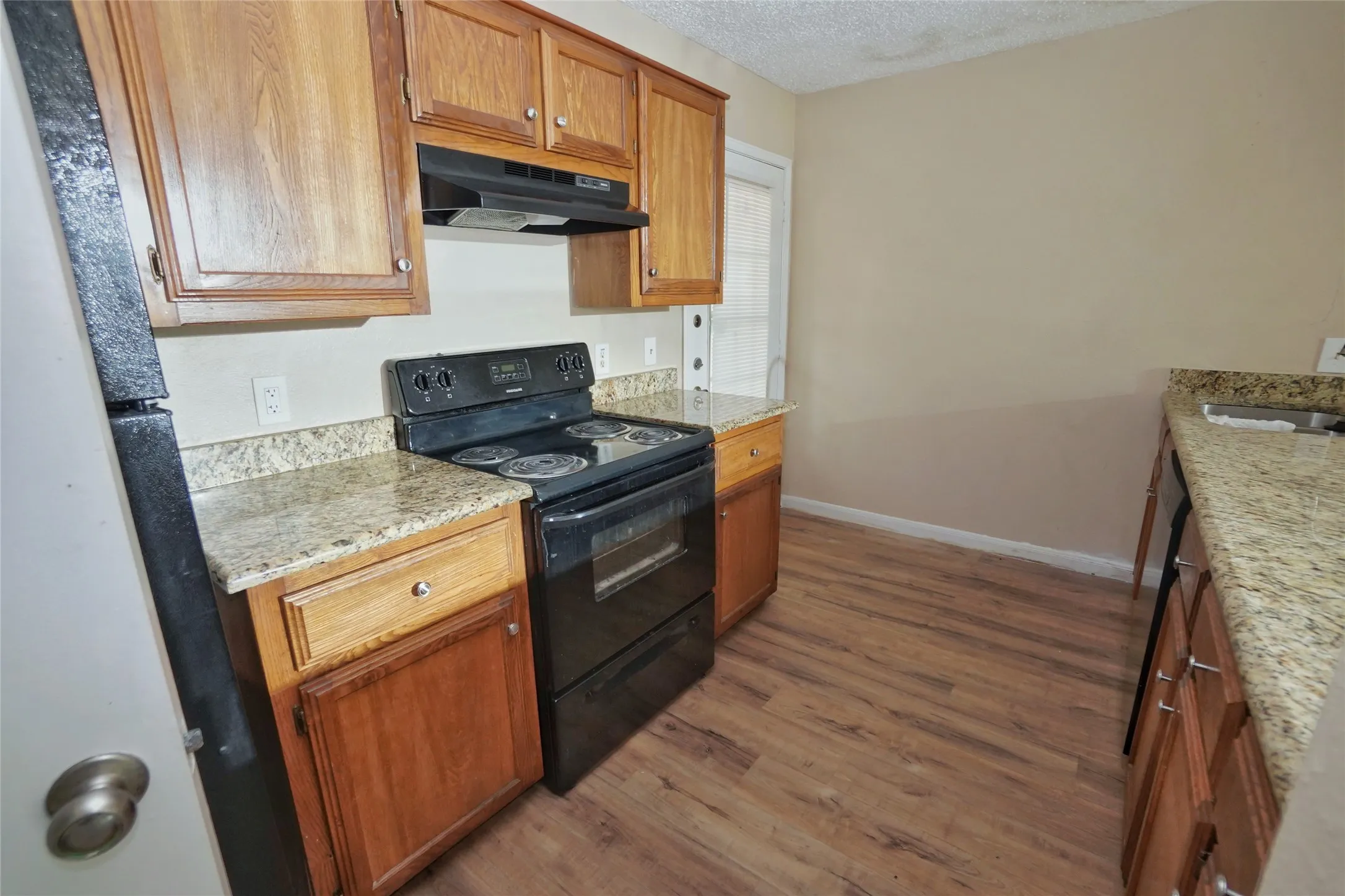 Kitchen featuring granite-style countertops, wood-finish flooring, wood cabinetry, and a black electric range with an overhead vent