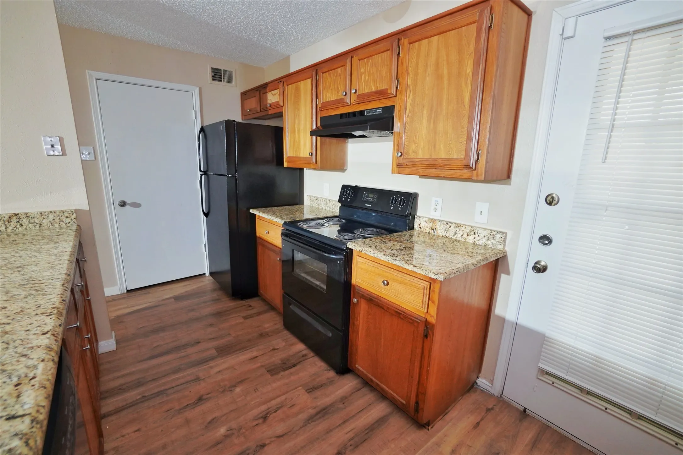 Wood-finish flooring with light-toned cabinetry, granite-style countertops, and a black appliance package