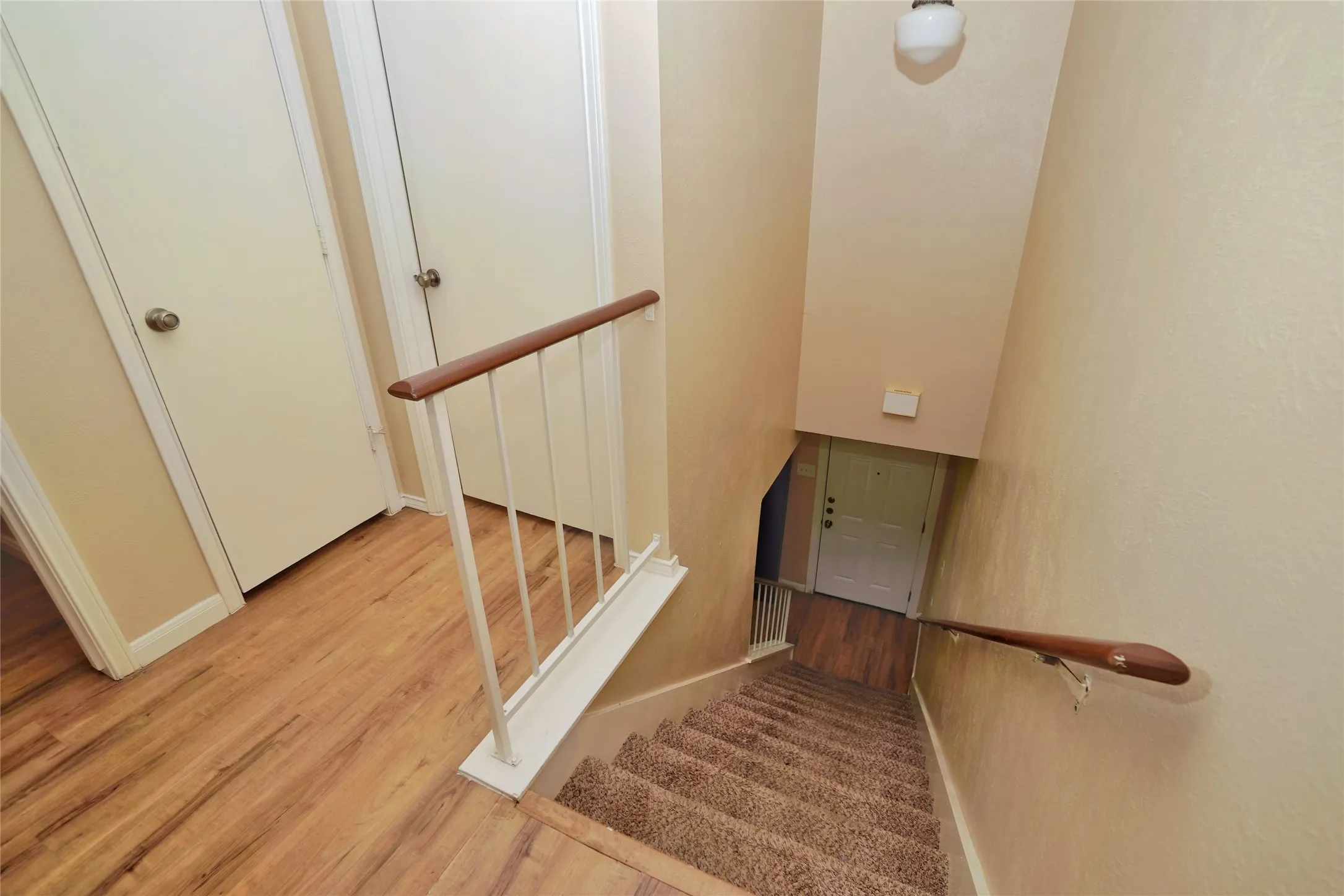 Wood-finish flooring, neutral wall tones, white interior doors, wood handrails, and a carpeted staircase