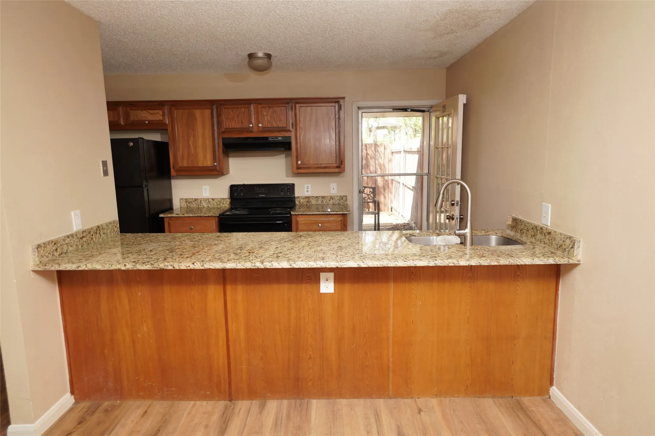Kitchen featuring wood cabinetry, granite-finish countertops, stainless steel sink with high-arc faucet, and black appliances