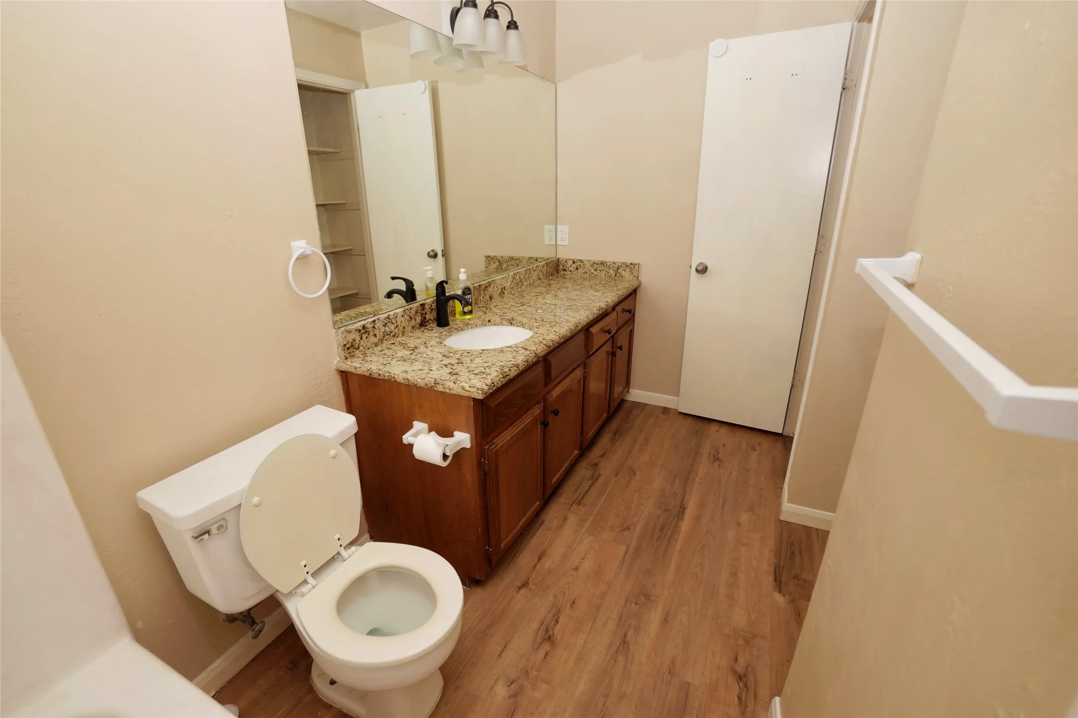 Wood-finish flooring, single vanity with a granite-style countertop, and built-in shelving