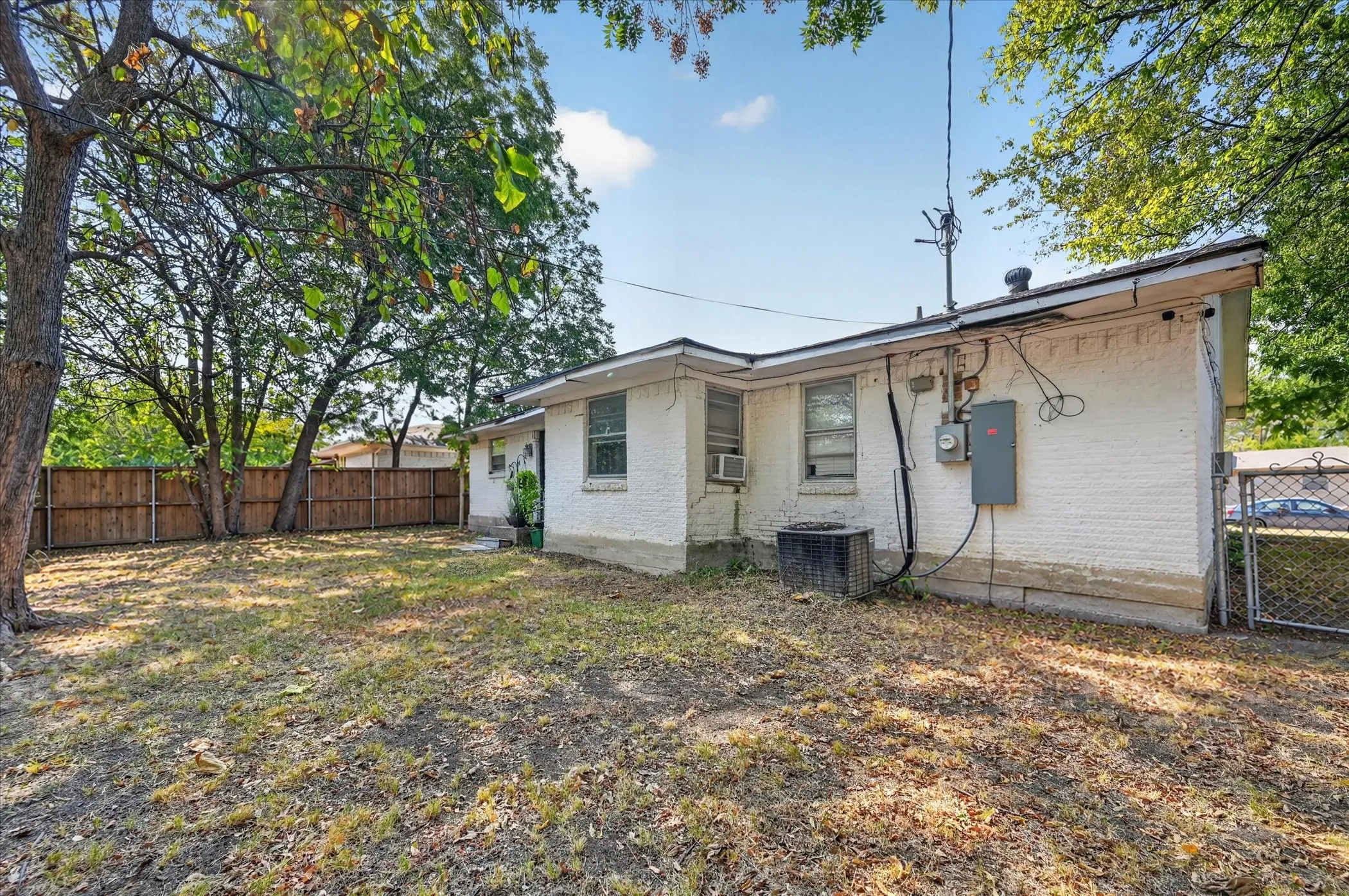Expansive rear yard with a wood privacy fence, mature trees, and a white brick exterior
