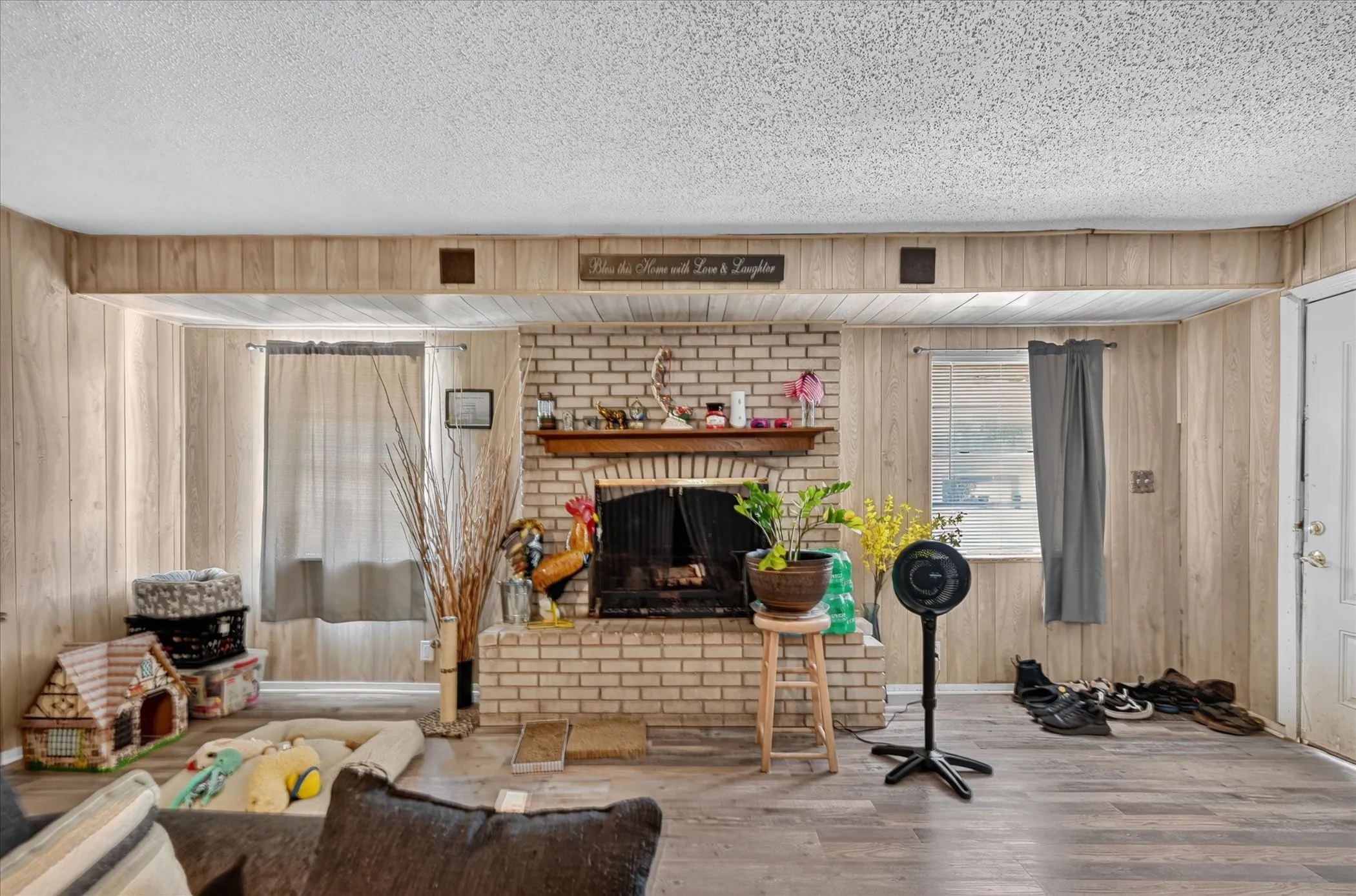 Brick fireplace with wood mantel, plank wood-finish flooring, wood paneling, and an exterior door