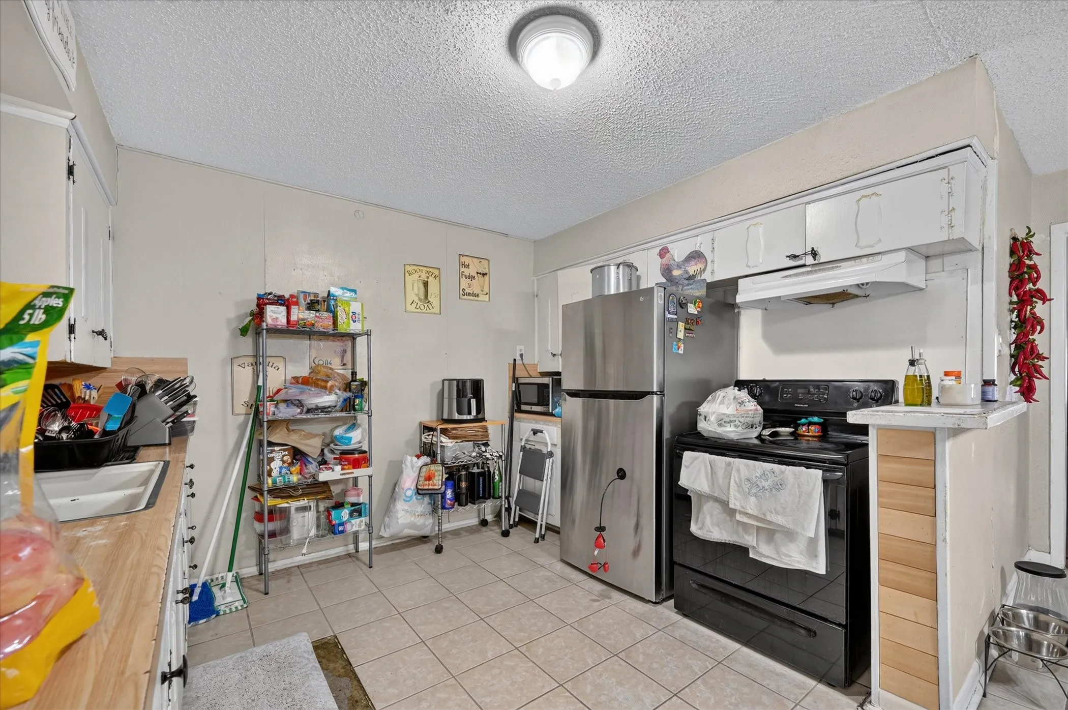 Kitchen featuring durable tile flooring, white cabinetry, wood-finish countertops, stainless steel refrigerator, and a black range