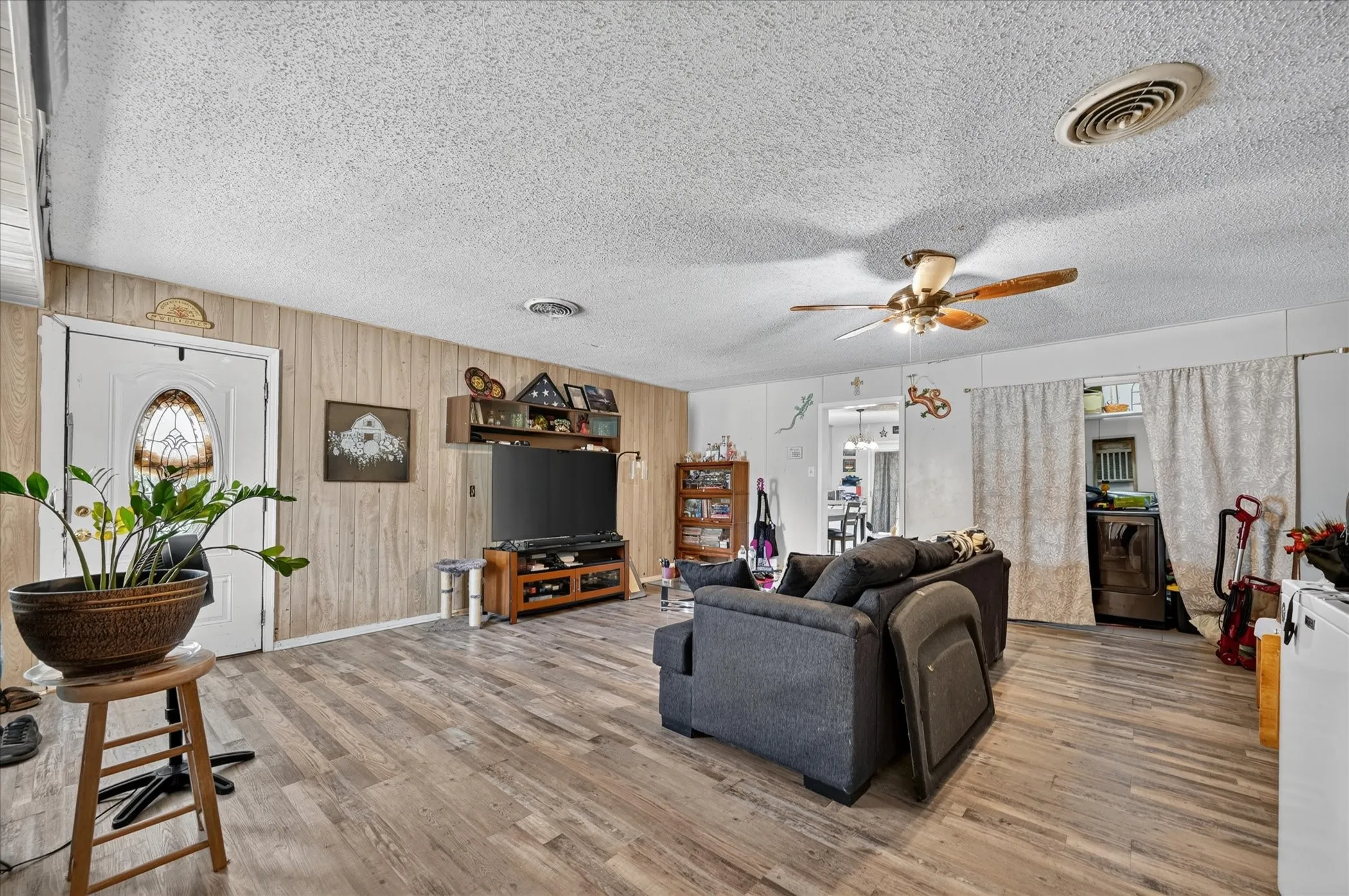 Wood-finish flooring throughout, white paneled entry door with an oval stained-glass insert, and a ceiling fan with integrated lighting