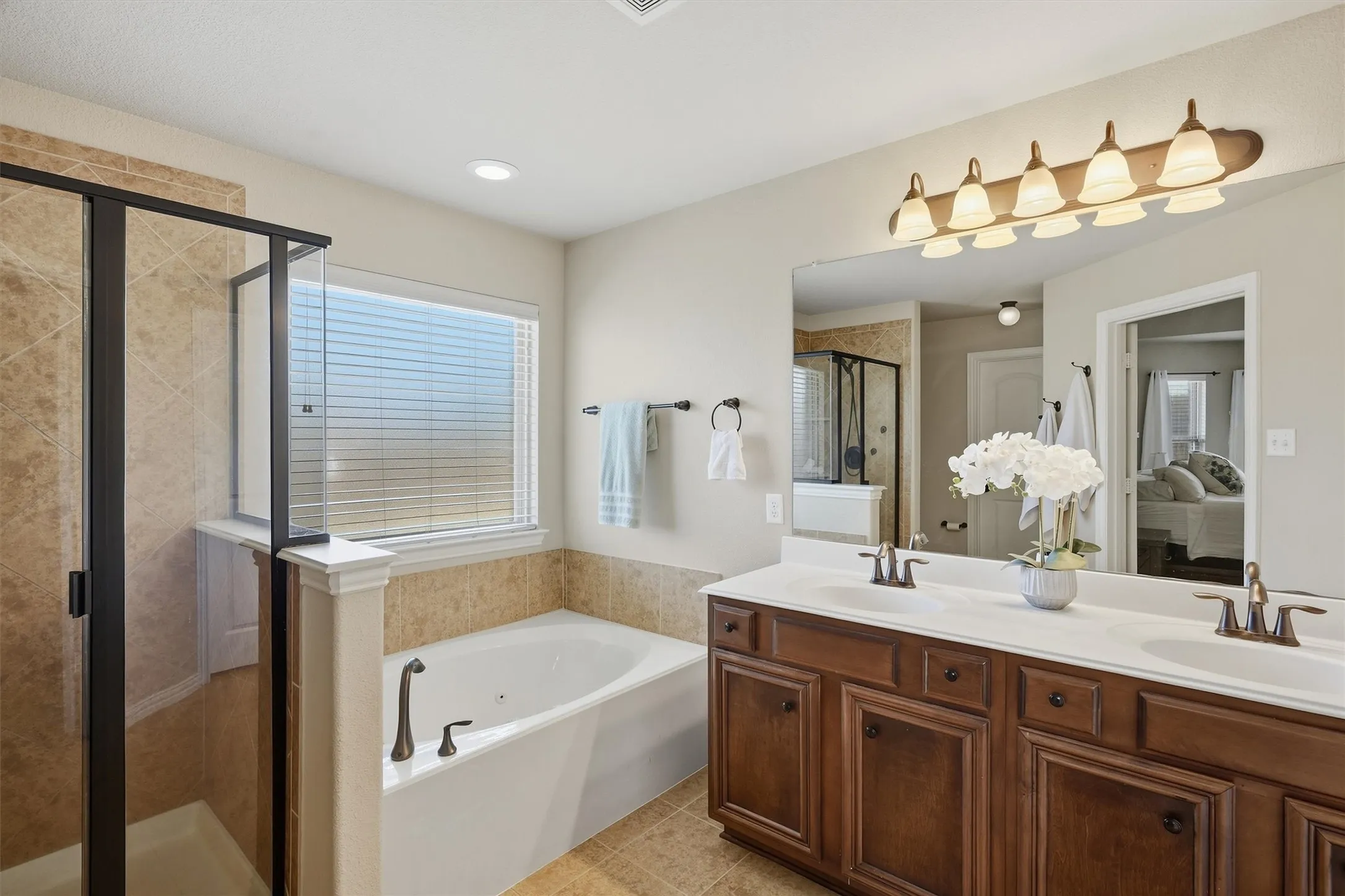 The primary bathroom features a dual-sink vanity with warm wood cabinetry, a deep soaking tub, and a separate glass-framed walk-in shower. Dual walk-in closets located off the ensuite provide generous, separate storage spaces for optimal organization.