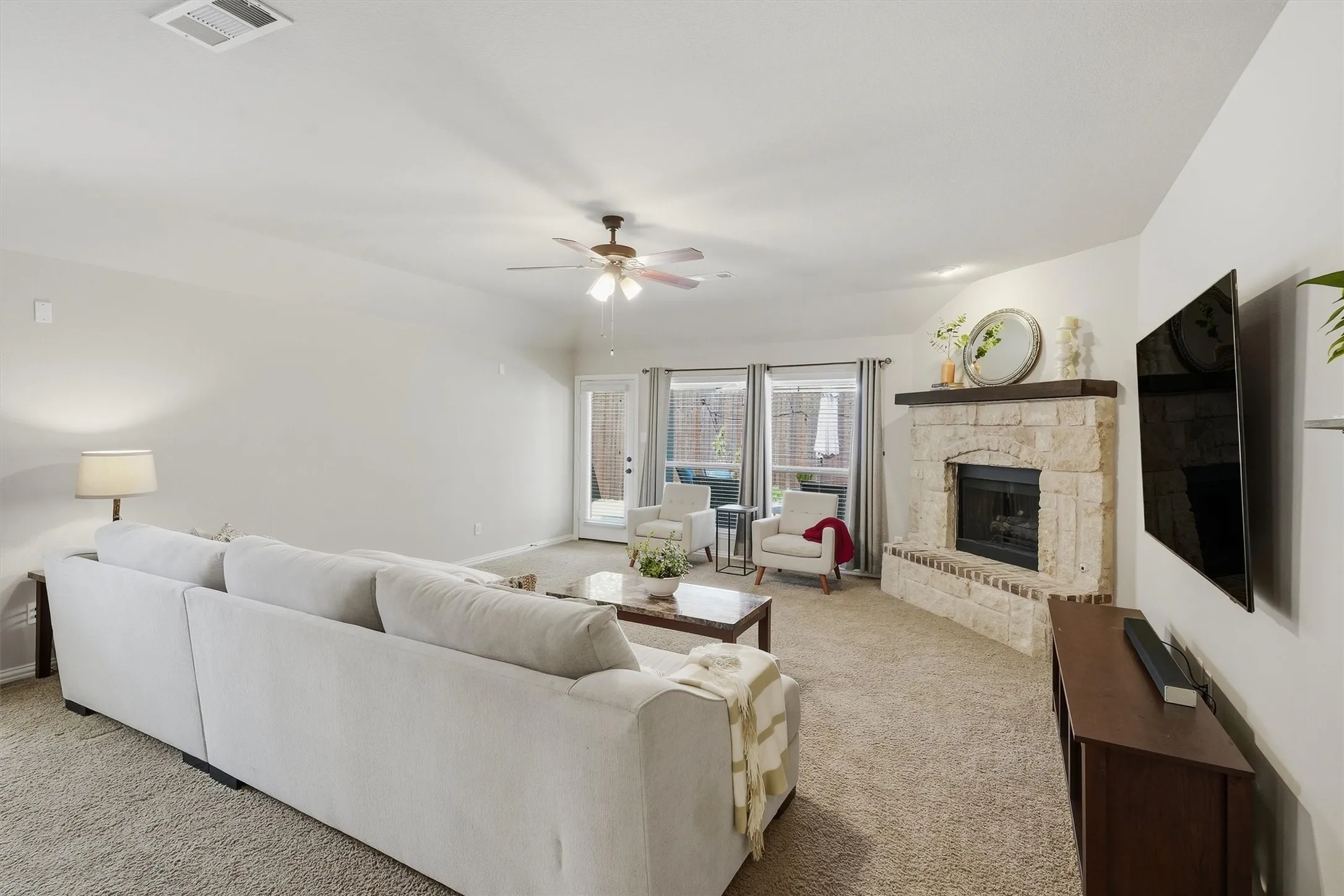 The living room showcases bright natural light filtering through the large windows and glass door leading to the backyard. High ceilings, a focal stone fireplace, and ample wall space for media setup make this a welcoming room for daily relaxation.