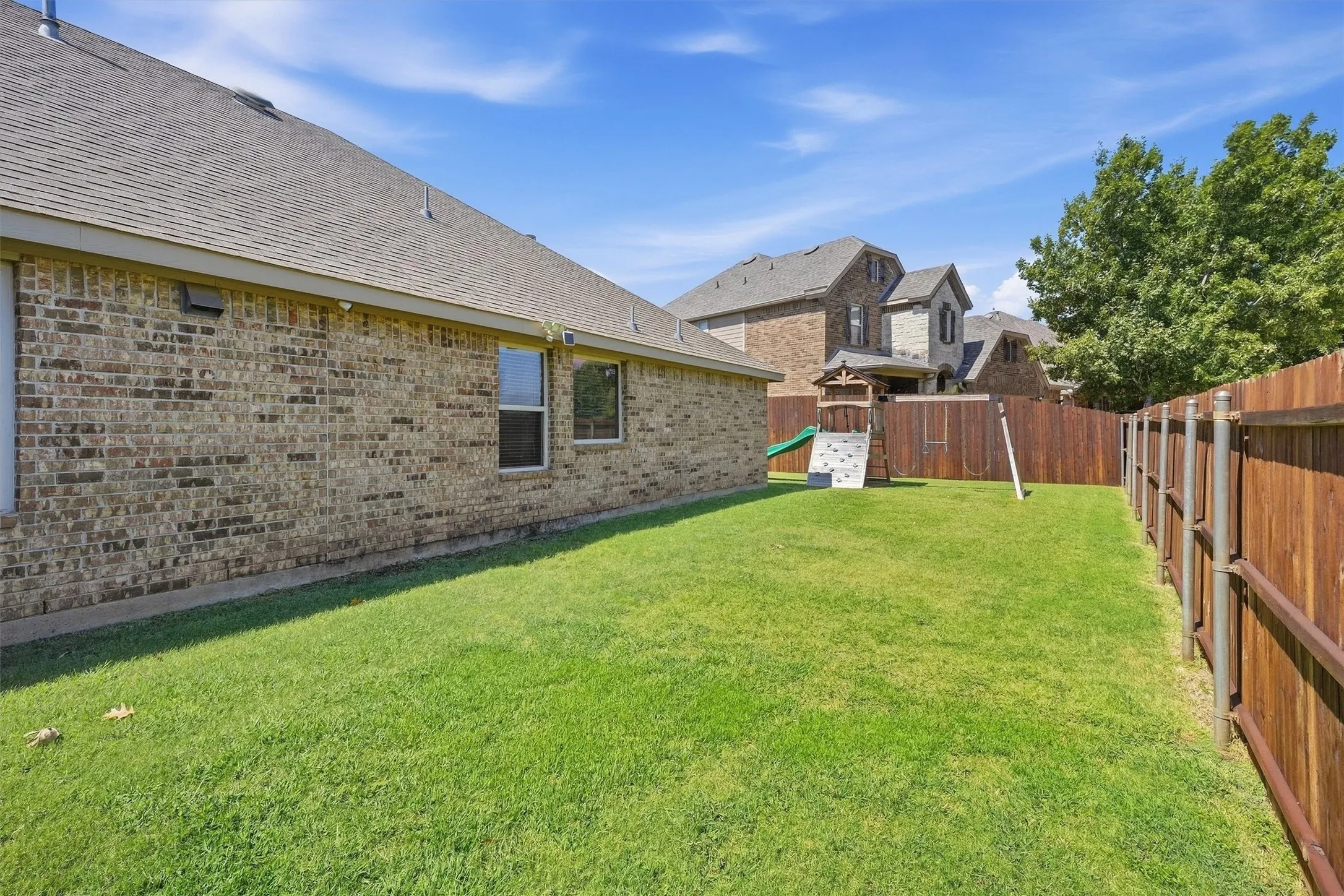This view along the side yard highlights the newly raised 8-foot privacy fence, offering extra seclusion and security for the lawn and backyard play area.