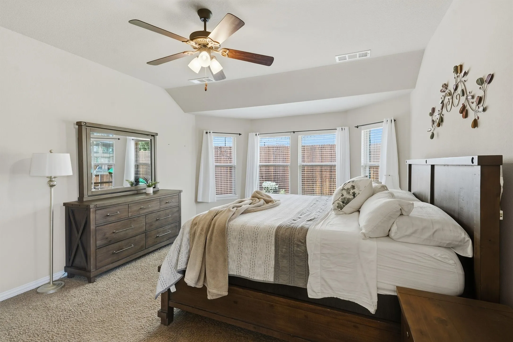 The spacious primary suite features vaulted ceilings, a lighted ceiling fan, and a charming bay-window nook that fills the room with natural light. Plush carpeting and soft neutral tones complete this comfortable, relaxing retreat.