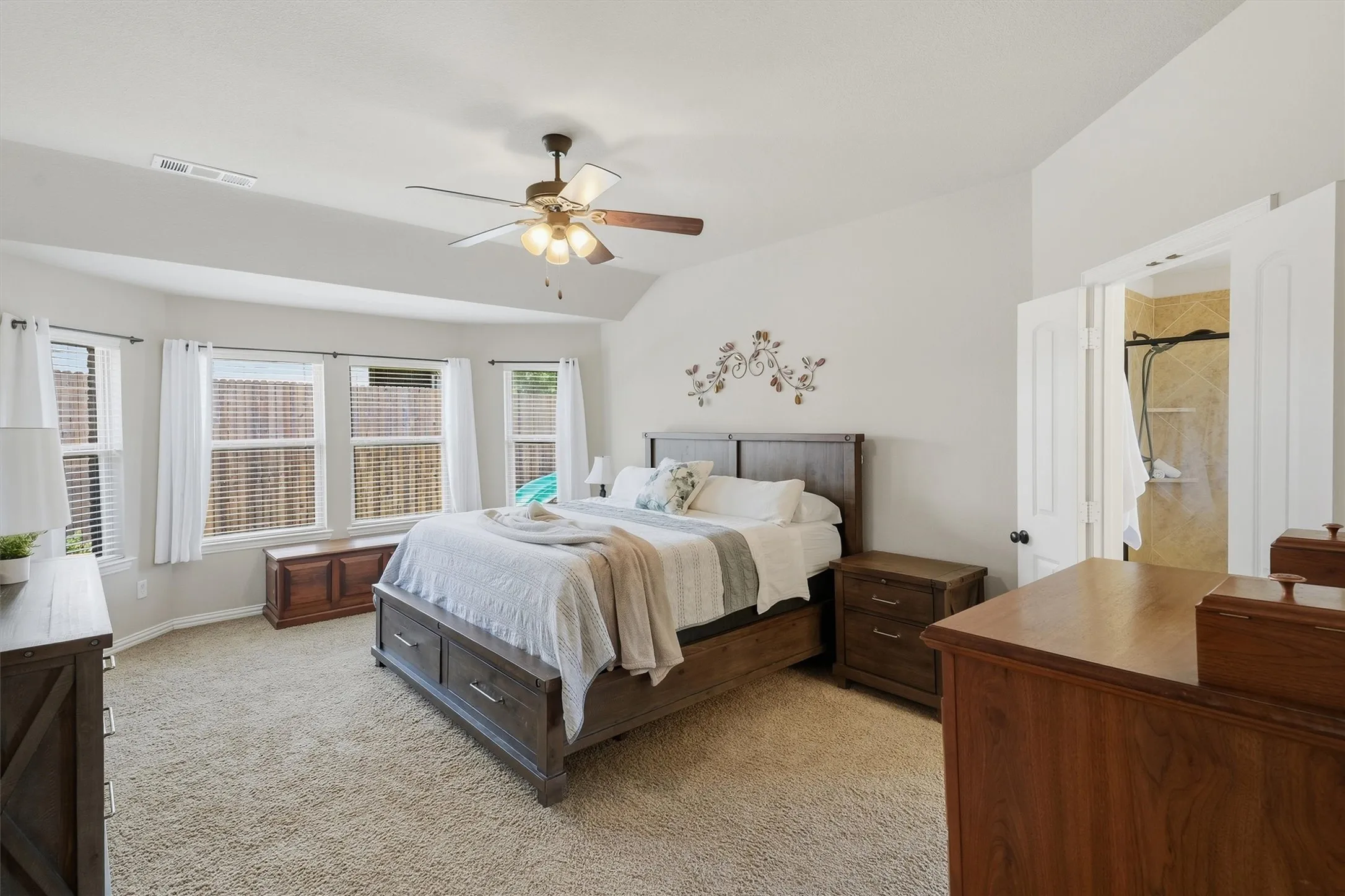 Another view of the primary suite demonstrates its impressive scale, high ceilings, and double-door entry into the private ensuite bath. A row of windows in the bay nook offers pleasant views of the backyard while letting in rich natural light.
