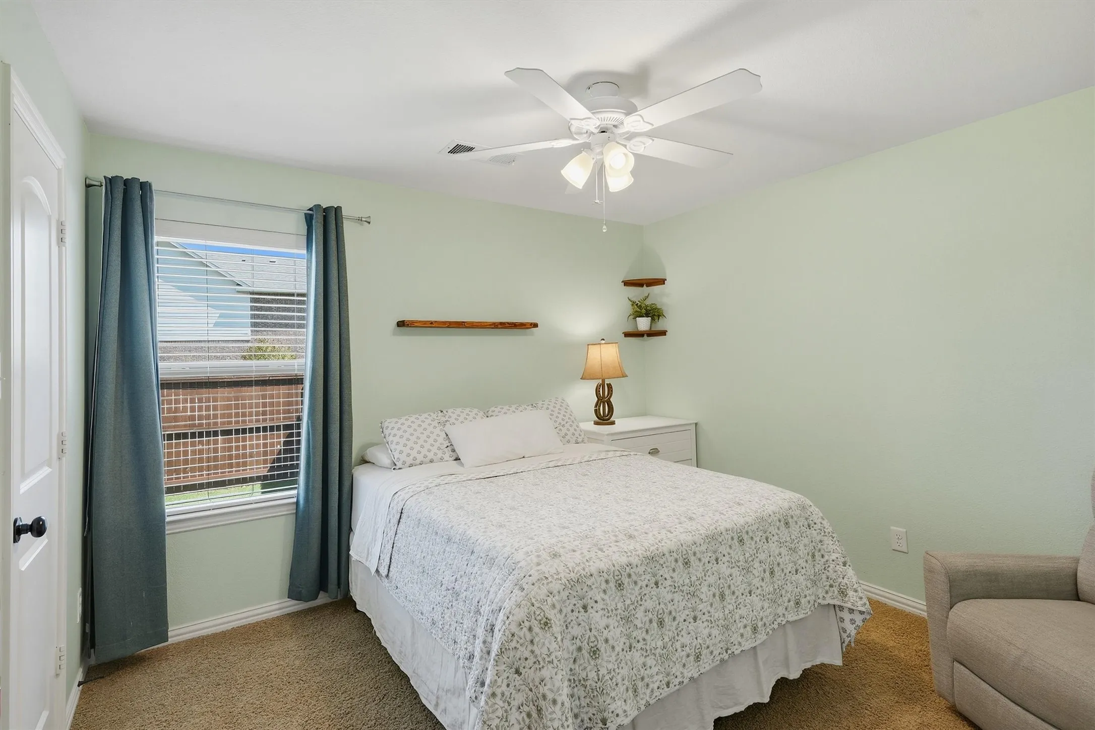 Soft mint green walls create a calm atmosphere in this spacious secondary bedroom, featuring a white lighted ceiling fan and natural light.