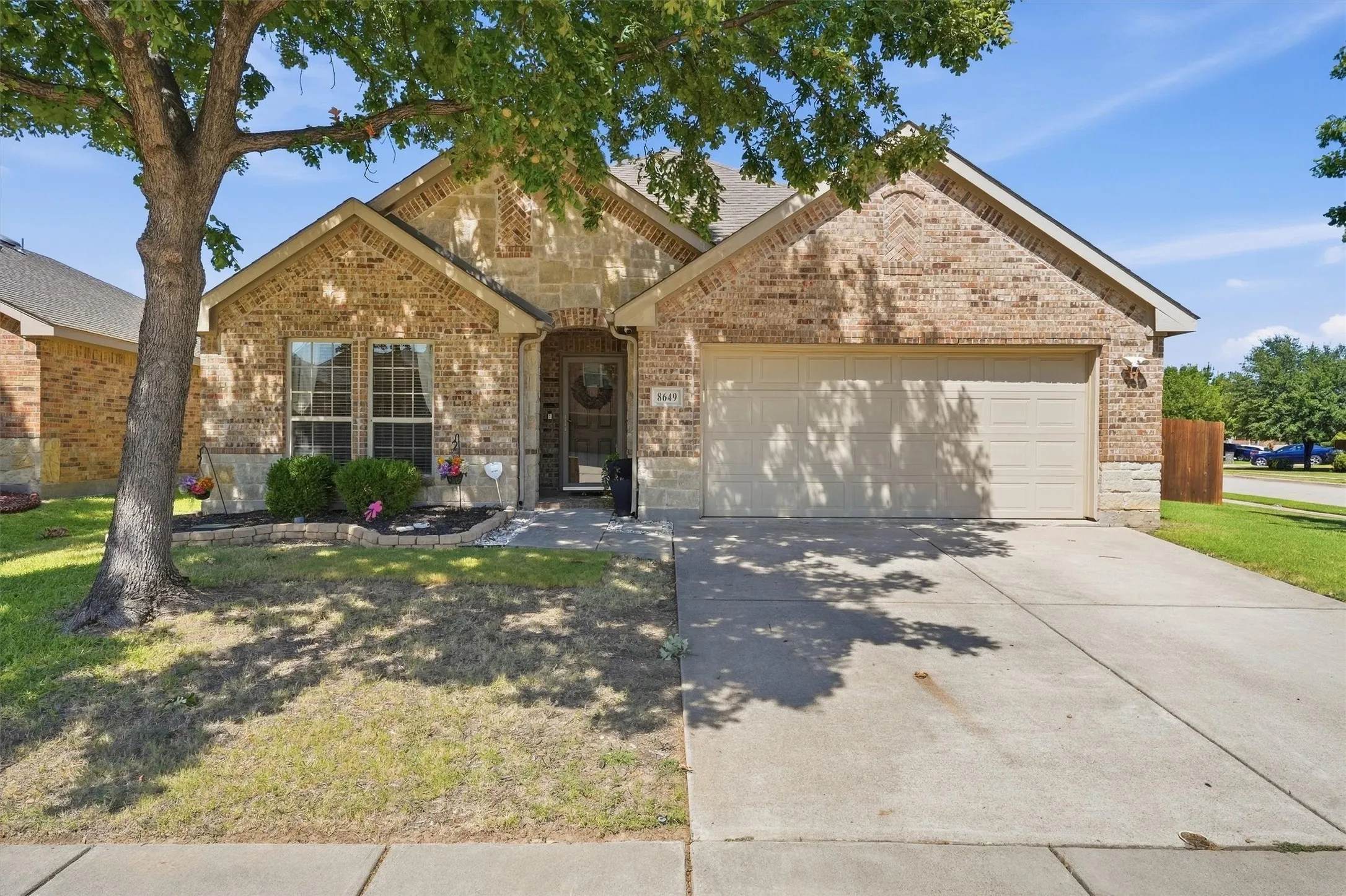 This home boasts striking curb appeal with a classic brick-and-stone exterior, a two-car garage, and a lush front lawn shaded by a mature tree.