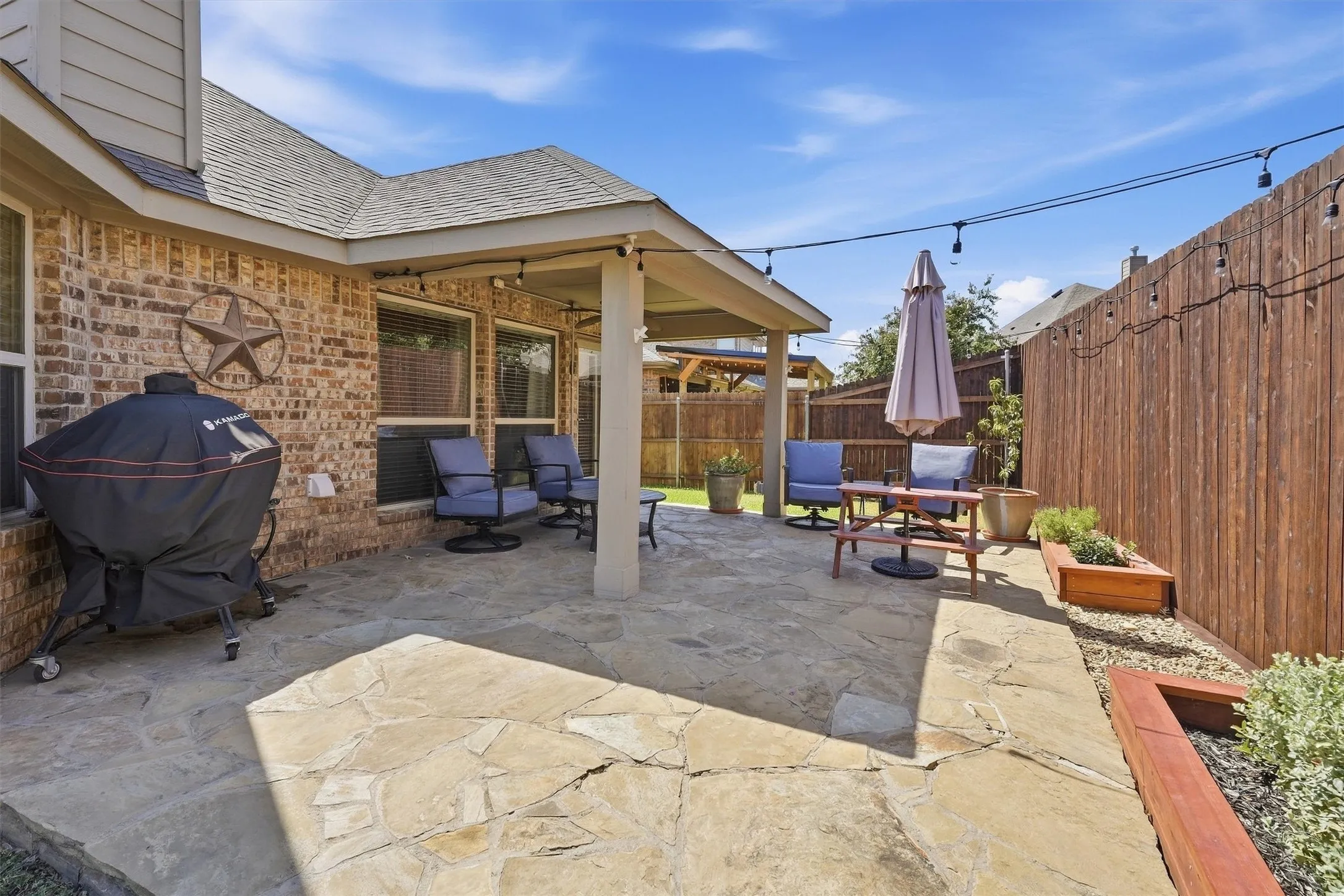 The stone flagstone patio expands outdoor living space, featuring string lighting, raised garden boxes, and plenty of room for grilling and lounging.