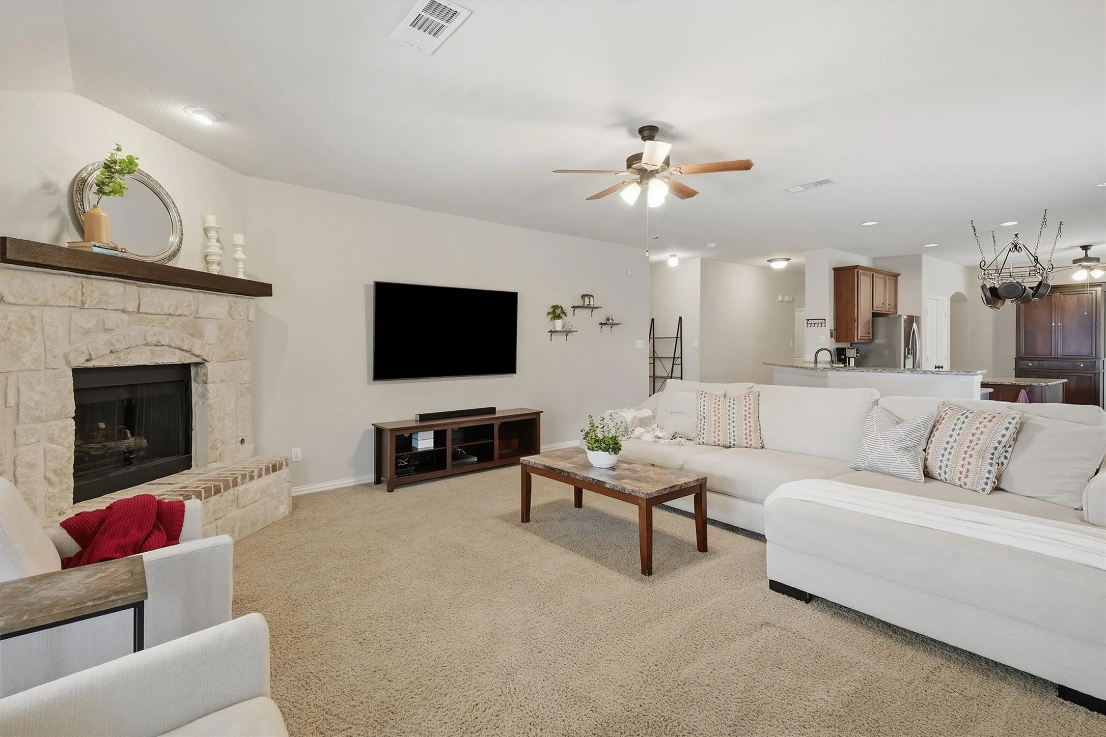 The inviting living room centers around a handsome floor-to-ceiling stone fireplace with a wood mantle. Neutral carpeting, recessed lighting, and a open flow into the kitchen create a warm and cohesive main gathering space.