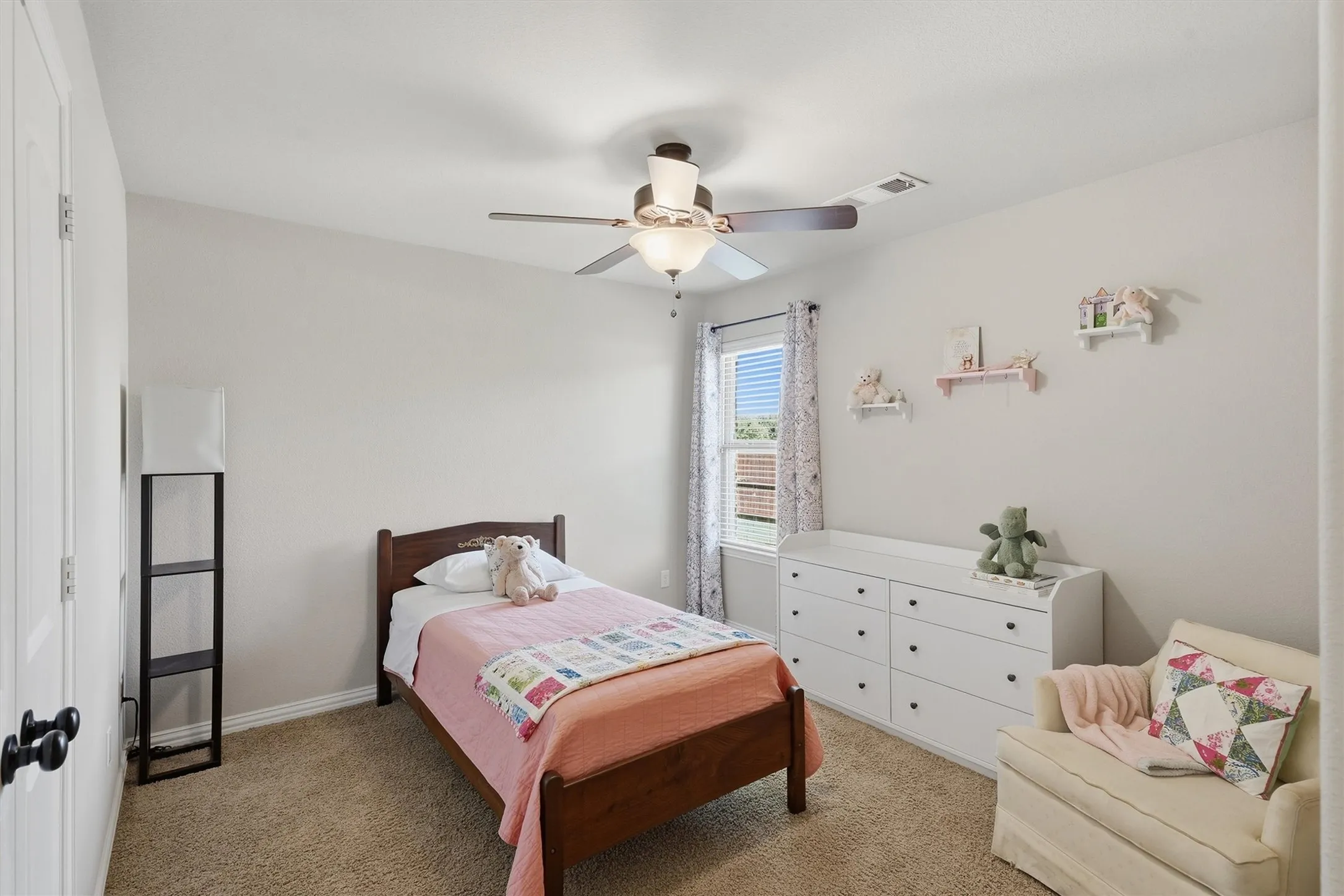 This bright secondary bedroom features neutral wall tones, soft carpeting, a lighted ceiling fan, and a window allowing for plenty of natural light. Generous wall space and built-in closet access make it a comfortable retreat for children or guests.