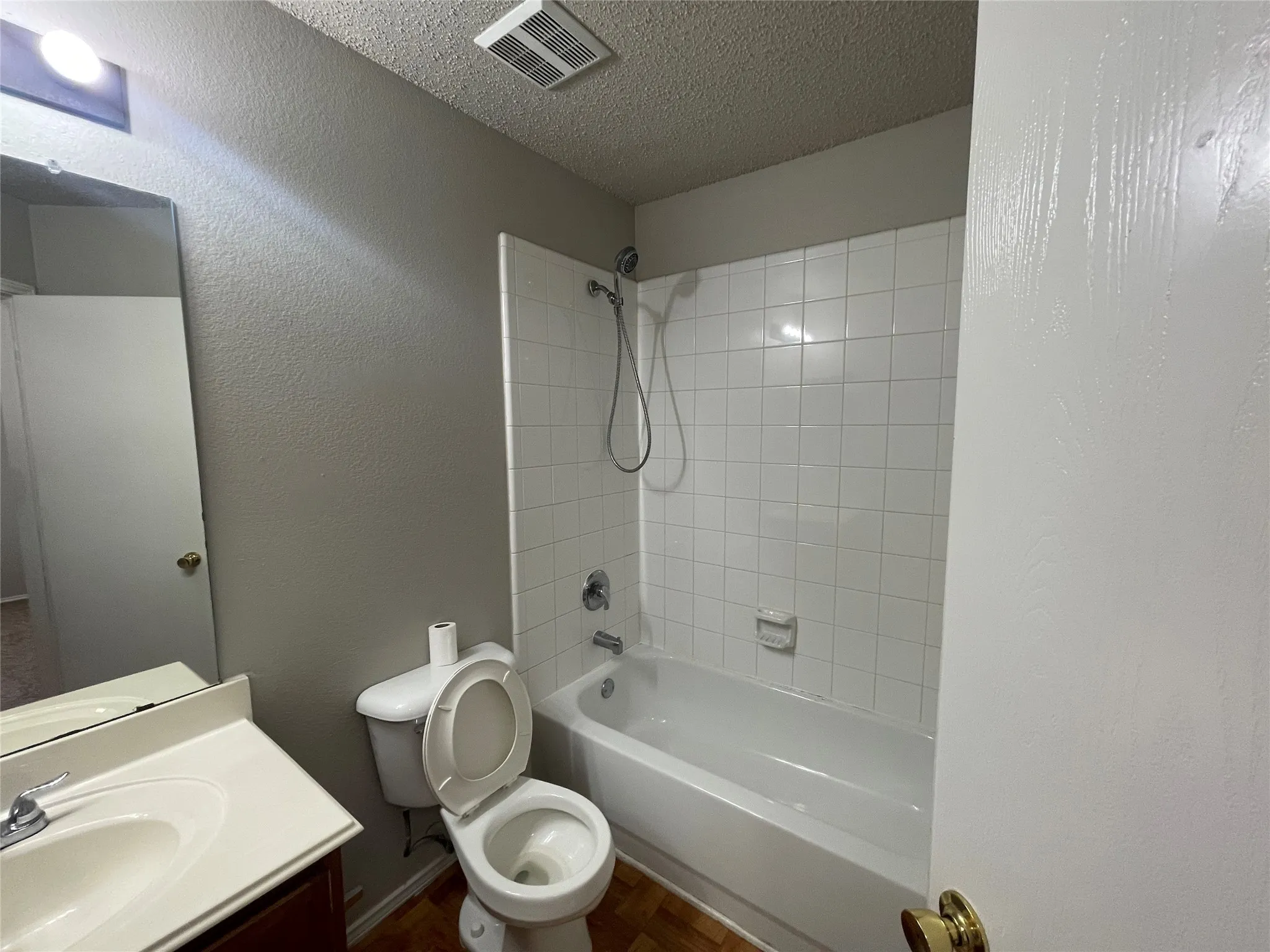 Bathroom with wood-finish flooring, white tiled shower surround, and a vanity with an integrated sink